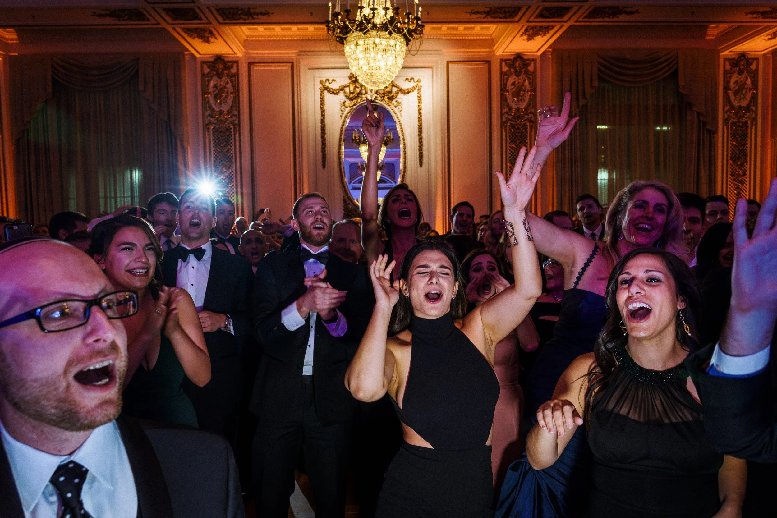 People dancing and singing at an elegant event in a decorated ballroom.
