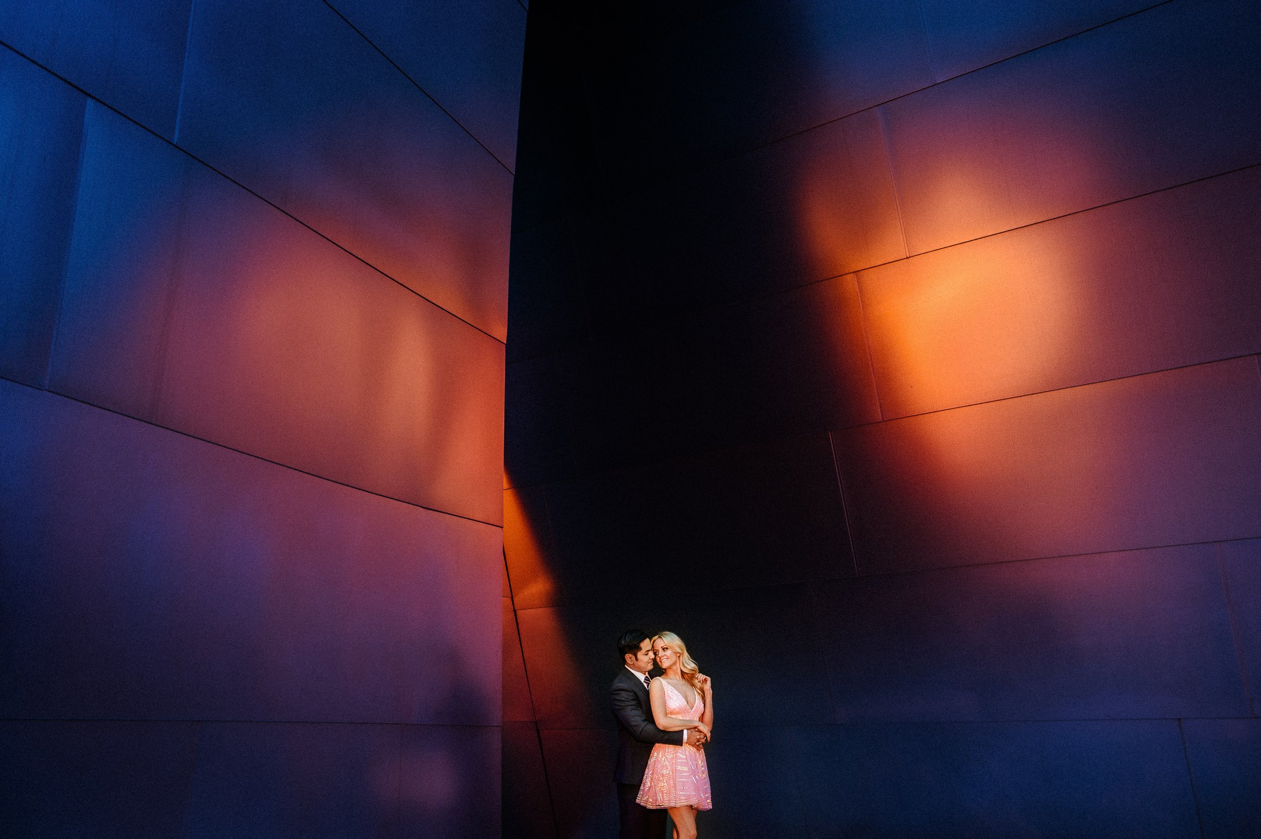 A couple dressed in formal attire standing close together at Walt Disney Concert Hall in Los Angeles during their engagement session.