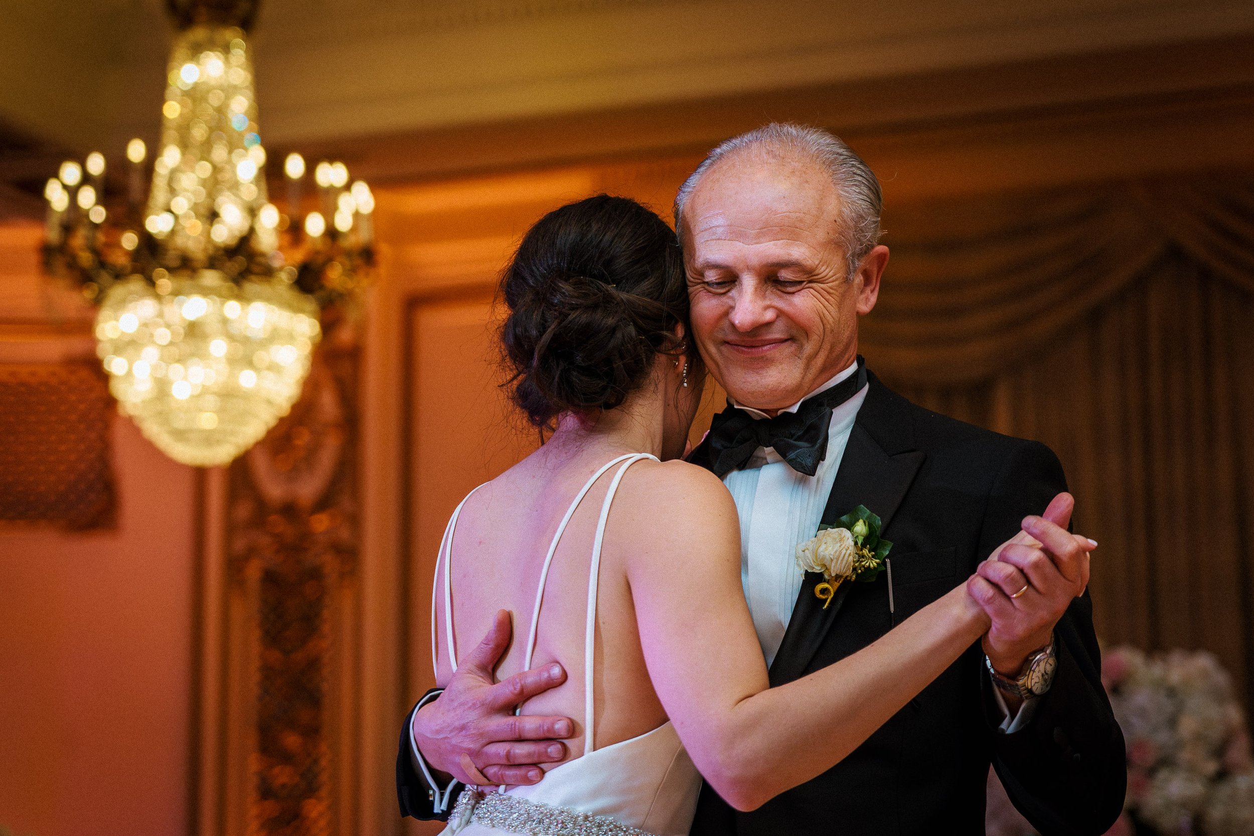 A bride and her father, are dancing closely at a wedding celebration. They are dressed formally, with the man in a tuxedo and the woman in a wedding dress, sharing an emotional moment.