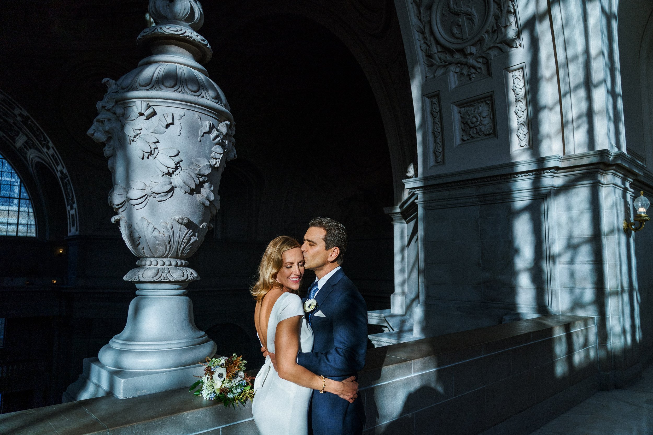 A couple dressed in wedding attire standing close at the San Francisco City Hall.
