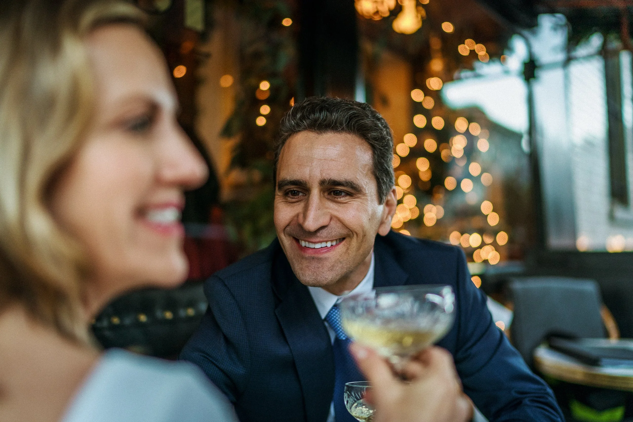 A man and a woman smiling and enjoying drinks at a decorated, cozy restaurant or bar.