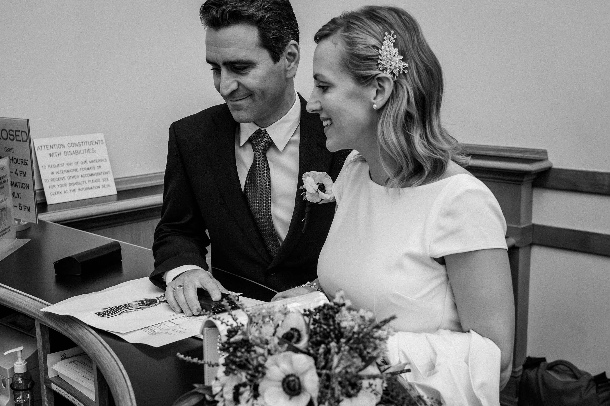 A bride and groom at their wedding, looking at a document on a desk.