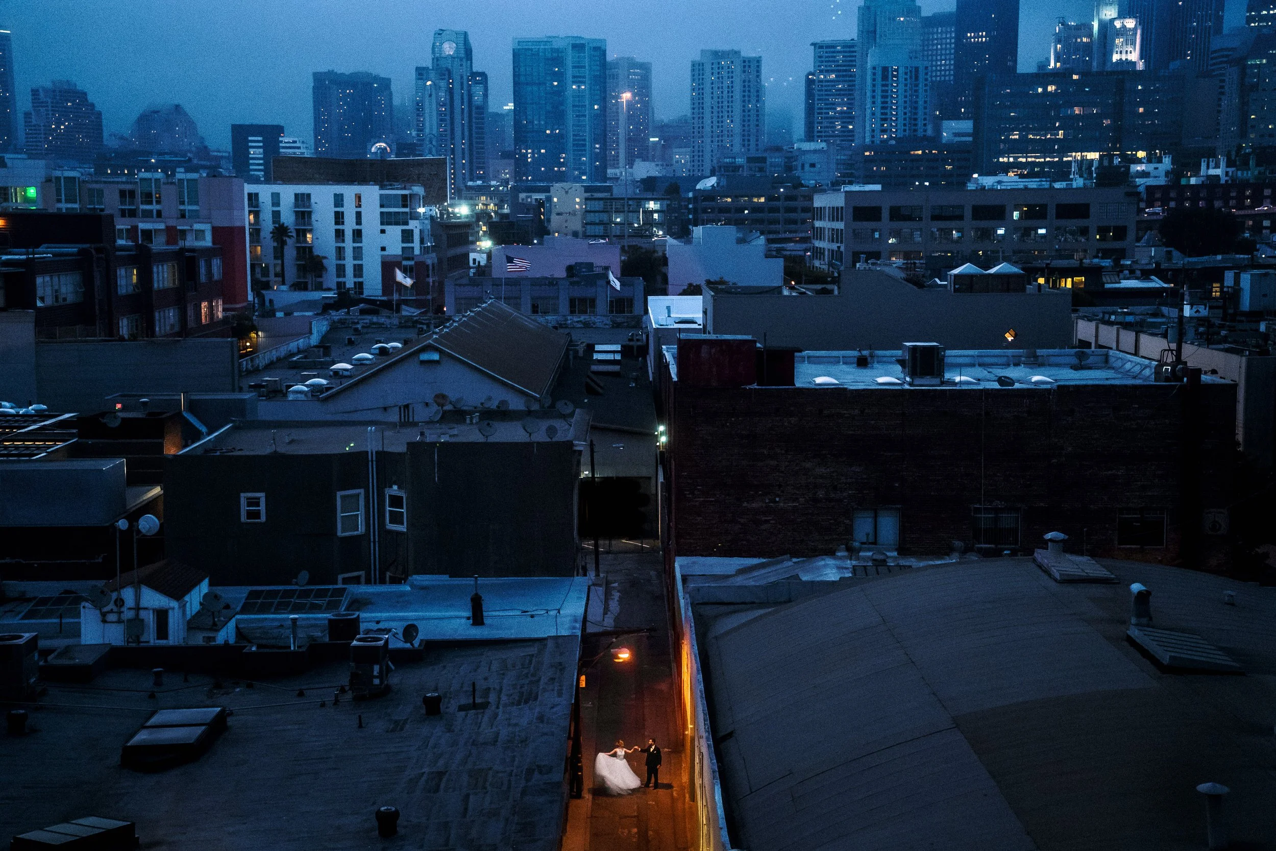 San Francisco skyline at dusk with tall buildings, and a narrow alley with a wedding couple dancing under streetlights below.