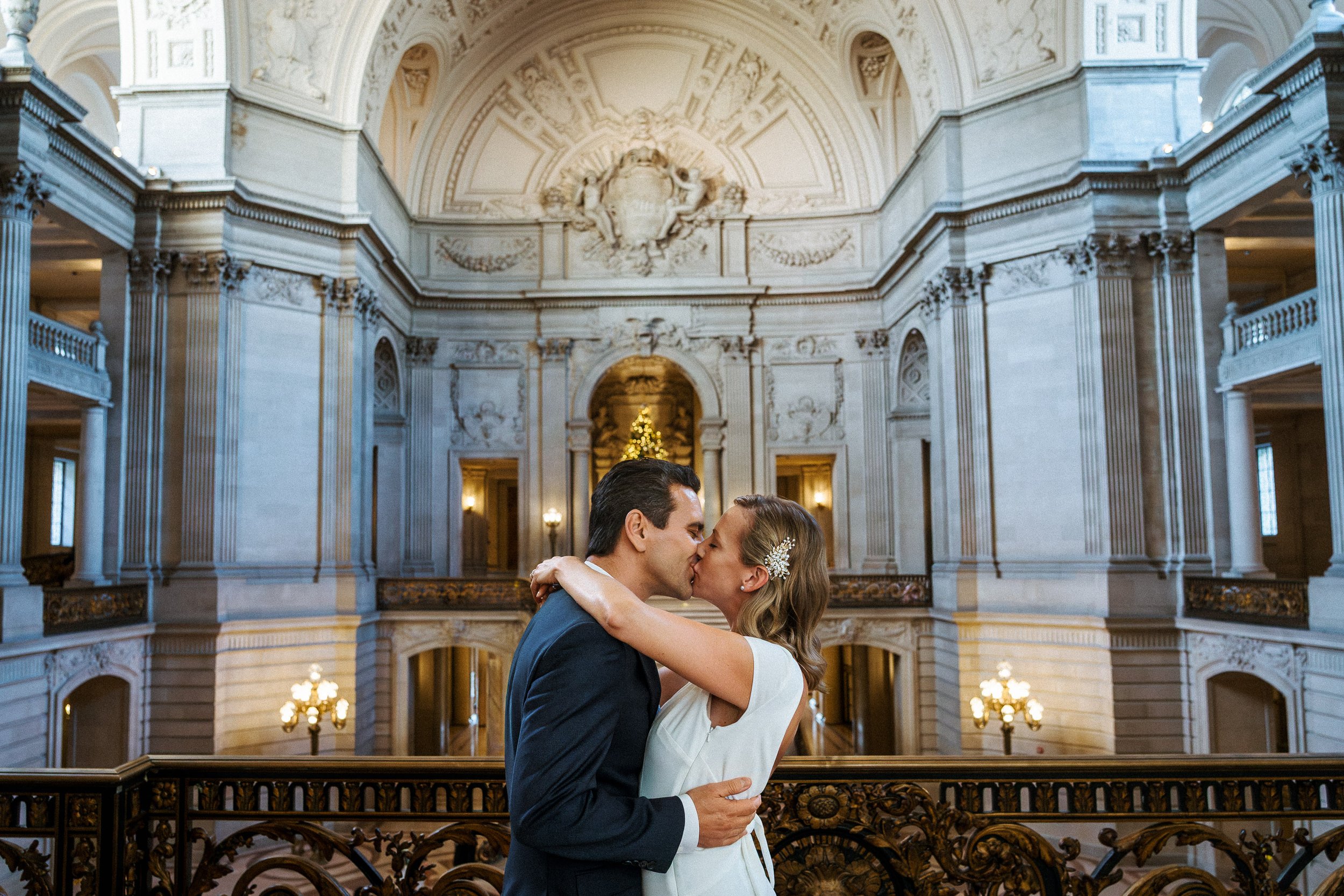 A couple kissing at the San Francisco City Hall with a Christmas tree in the background.