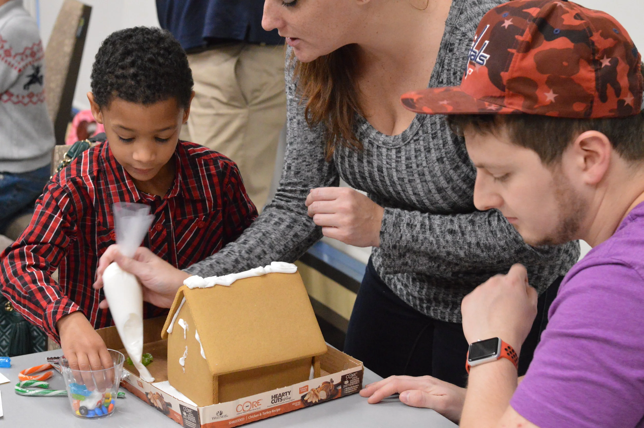 Three people decorating a gingerbread house at a table