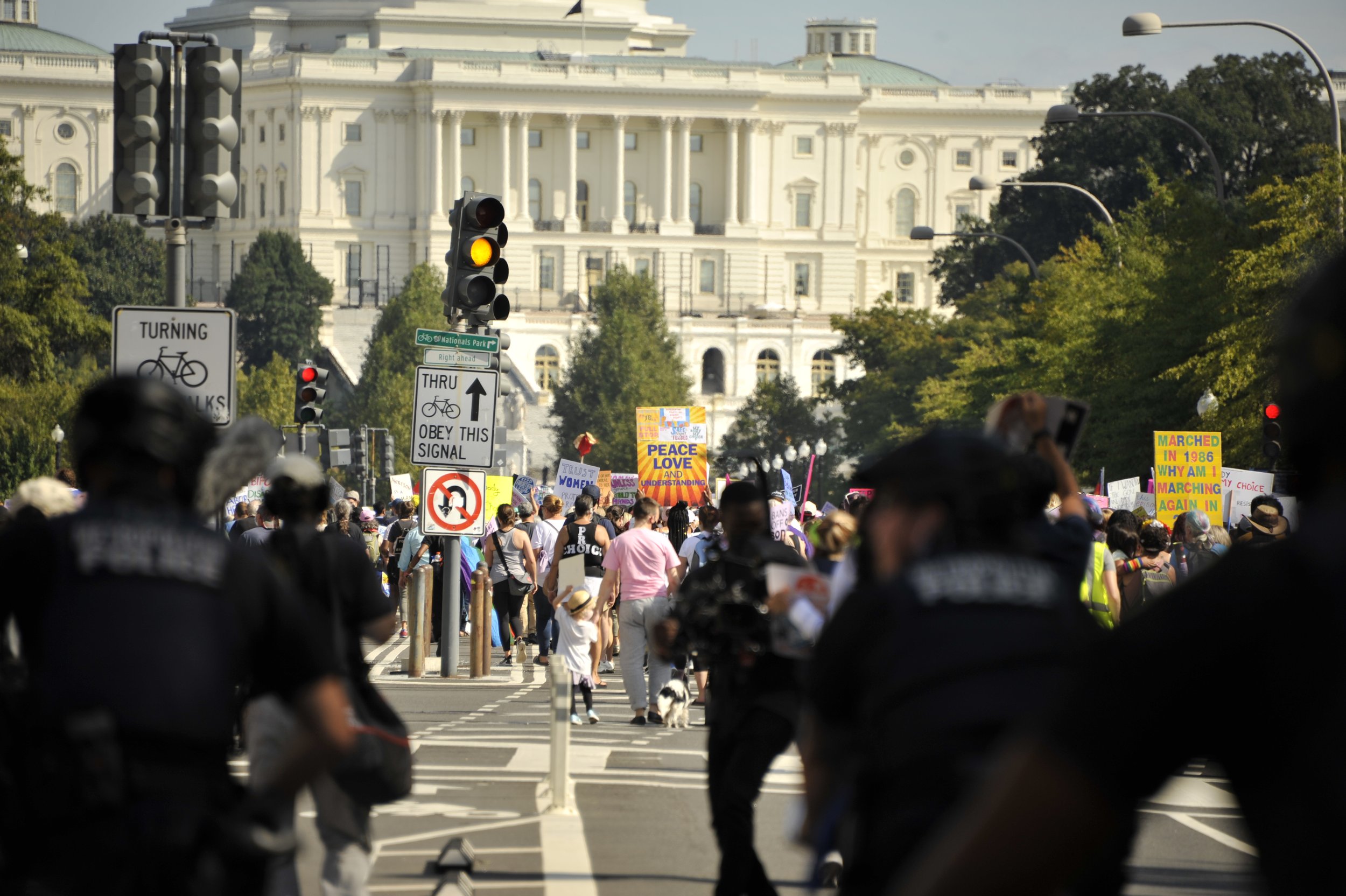 Crowd of protesters and police officers with the White House in the background, holding signs and banners during a demonstration.