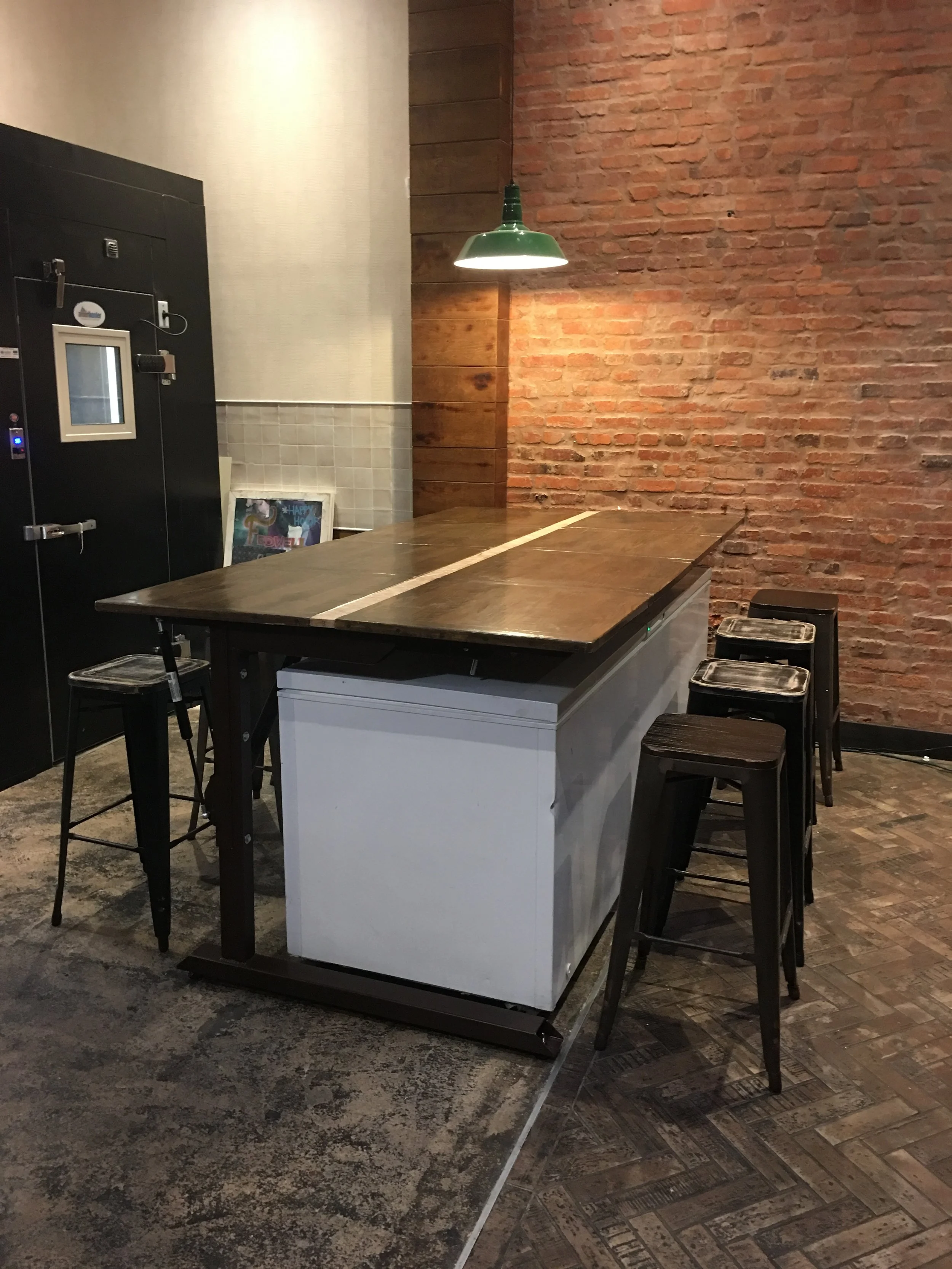 A large cantilevered table with a liftable top to allow access to an industrial chest freezer underneath.