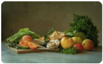 Fresh vegetables and herbs on a wooden cutting board on a marble countertop.