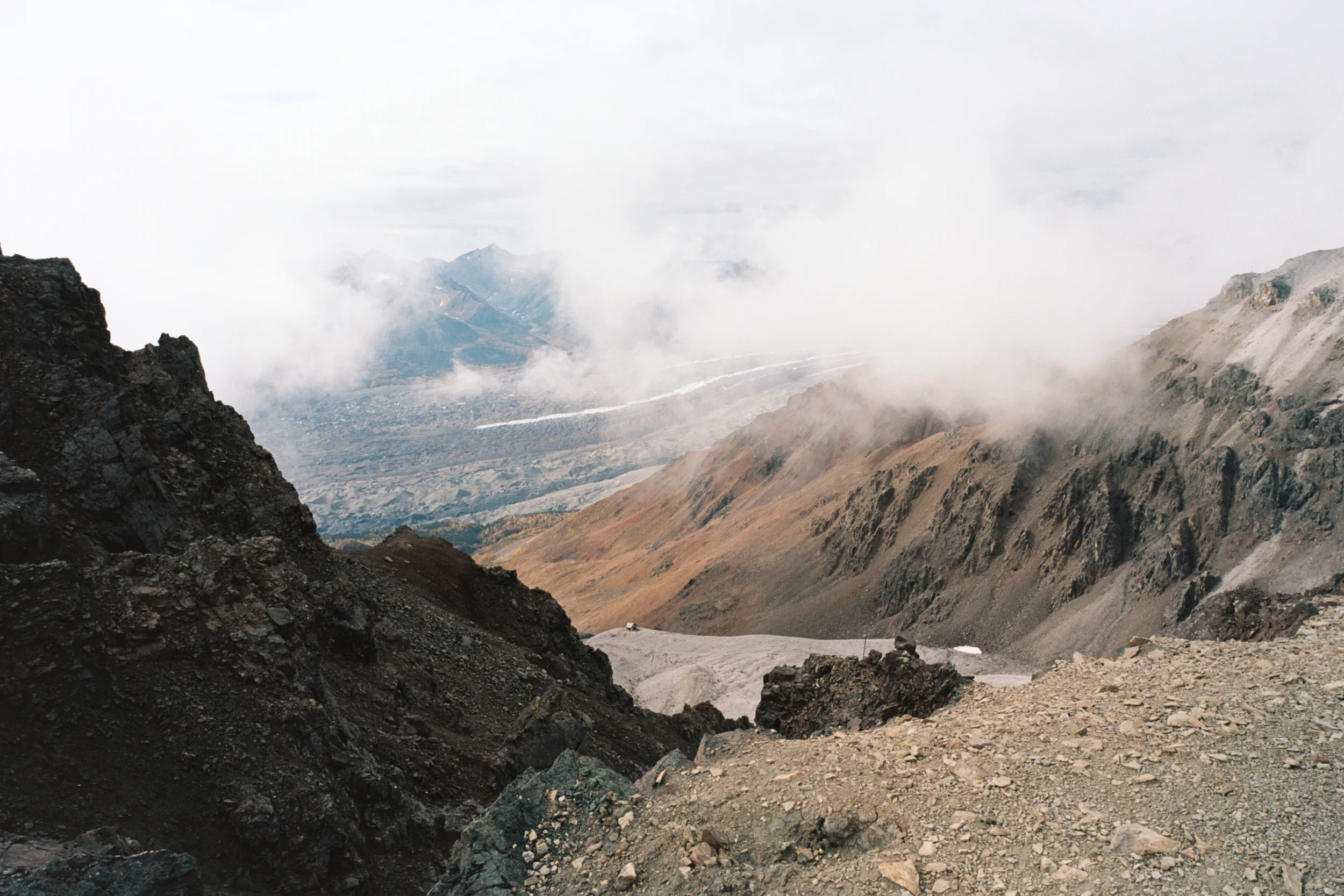 Looking down at Kennecott Glacier in the distance (the glacier is covered with a lot of earth, but you can see lines of clean ice running down it). In a small valley just below us sits a small abandoned mine building.