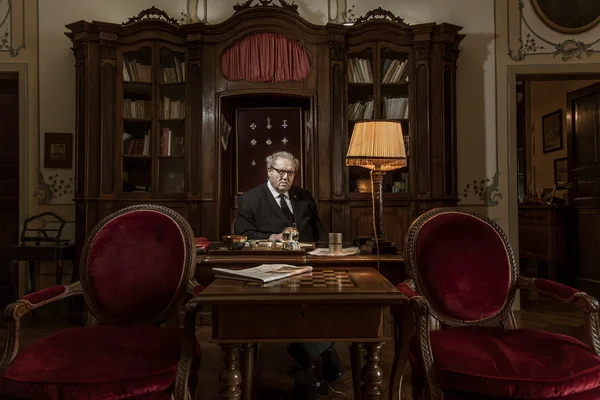 At Home with Matthew Festing, Grand Master of the Knights of Malta  The ex-soldier is Grand Master of a Catholic fraternity that was founded in the 11th century and carries out aid work in 120 countries   By Hannah Roberts   The private residence of the Grand Master of the Knights of Malta is perched high above the Ligurian Sea on a rocky promontory near Rapallo and within view of the mouth of Portofino harbour.  A Maltese Cross flies from the battlements of Villa Pagana, or Villa Malta, as the locals have called it since the 1950s, when the Spinolas, a family of princely merchants, entrusted it to the world’s oldest surviving chivalric order.  The Sovereign Military Hospitaller Order of Saint John of Jerusalem of Rhodes and of Malta (to give it its full name) is an enigmatic Catholic religious fraternity founded in 1048.  Despite having no territory, it is considered a sovereign entity under international law, printing its own postage stamps and coins.  A butler, in a white jacket with gold buttons, leads me into the salone, where I await His Most Eminent Highness The Prince and Grand Master of the Knights of Malta, also known as Matthew Festing, a former Grenadier Guardsman from Northumbria in England.  I was briefed to “present formally”, as befitting an encounter with a head of state but, disappointingly, Festing is in mufti, consisting of a blue jacket and green trousers, rather than his ceremonial black cloaking.  The former Sotheby’s consultant took possession of the ochre villa — surrounded by maritime pines and an exotic garden of cacti, palms and orange bird-of-paradise flowers — in 2008 when he was appointed as the order’s 79th Grand Master. Festing was elected for life in a secret ballot at a papal-style conclave in Rome and has both a ceremonial and decision-making role overseeing its humanitarian activity. He does not draw a salary although his living costs are met.  Festing plays down the grandeur. “You would think, gosh, it’s an enormous house, you can have 25 people to stay, but you’d be pushed to have more than six. It’s a family home really.”  Aged 66, he has not married or had children — as one of about 60 professed knights, he has taken a vow of celibacy, as well as of poverty and obedience. But his great-nieces and nephews visit in the summer, playing in the tower and cruising in his 1960s Ligurian fishing boat.  The villa was built in the early 1600s, with a watchtower as defence against any attack from French-Piedmontese troops. An antique brass telescope stands at a first-floor window, pointing out to sea as if anticipating a raid.  Historically, members of the order have been descended from European nobility. Festing traces his family back to 14th-century knights. His ancestor, Sir Adrian Fortescue, a cousin of Anne Boleyn, was executed because he refused to sign an oath acknowledging Henry VIII as “Supreme Head” of the Church in England instead of the Pope.  We sit amid 17th-century Genovese furniture looking through wooden doors on to the chequered-floor terrace and the sea beyond. The room is replete with chandeliers, portraits of regional nobility and antique oddities, including a stuffed turtle and a harpsichord.  Behind a curtain is a chapel with red silk walls, six carved wooden pews, a green-painted altar and a spectacular view. Which for the local priest who says mass there every morning might be part of the attraction.  There are two staircases, the servants’ and the grand, both leading to the first floor where “Aeneas’ Escape from Troy” by the Neapolitan painter Luca Giordano (1634-1705) hangs in Festing’s office. “Gloomy but extraordinary,” he says. Previously it was on the dining room ceiling. “It was absolutely black but when it was cleaned all sorts of funny things appeared, like a dog in the bottom left-hand corner.”  Paintings were Festing’s first love during his years as Sotheby’s representative in Northumbria — he once found an unknown painting by Constable of a garden. “It was an extraordinary find. She, a perfectly ordinary lady, was the descendant of Constable’s neighbour, a Mr Gardener. Constable must have painted it and given it to him. So it was Mr Gardener’s garden.”  Festing, a hospitable fellow, offers a splendid lunch, saying grace in Latin before and after. We are served bresaola, orange and grapefruit salad, followed by saffron risotto with osso buco and then cheeses, accompanied by white wine.  The order was founded when a group of knights established a hospital to tend people of all faiths. The motives of these warrior monks were “complicated”, Festing admits. “Some were on a religious high, others were simply short of land.”  Because of their military training, the original knights also acted as a Christian militia, defending pilgrims from attack. They were driven out of Jerusalem in 1291, settling in Rhodes and then Malta, which they ruled until they were forced out by Napoleon in 1798.  Its territory lost, the order is now headquartered in Rome and draws on its charitable rather than military roots, operating humanitarian relief and medical missions in more than 120 countries. Almost 100,000 people work with and for the order, including more than 80,000 as volunteers. “It’s bigger than the British army,” Festing points out.  Some of its 25,000 doctors, nurses and paramedics run older people’s homes in England, schools for autistic children in France and homes for people affected by leprosy in Brazil. The order has been at the forefront of Europe’s refugee crisis, providing doctors on Italian coastguard vessels rescuing migrants in the Mediterranean. It also runs 70 emergency shelters and 30 registration centres with medical and legal facilities for refugees in Germany.  The order’s property portfolio pays for its central administration in Italy, but worldwide operations are decentralised and run by individual associations. Work is funded by donors such as the EU, government and international agencies as well as individuals — more than 1m in Germany and 1m in France. “They might be a little old lady who gives you five euros and they might be Mr Big who gives you 10,000 euros.”  As a sovereign entity, the order has a network of embassies, permitting diplomatic relations with 104 countries. Like Palestine, another stateless sovereignty, it has observer status at the UN. This unusual place in international politics, together with its mysterious practices and rituals, has provoked no shortage of Dan Brown-style conspiracy theories over the years, with some claiming that the order is a shadowy clique of modern-day Crusaders with a Christian supremacist agenda.  In 2008 the order was accused of links to Blackwater, the mercenary security group, a connection Festing’s predecessor robustly denied. There have also been (rebutted) claims that the former US commander in Afghanistan, General Stanley McChrystal, was a member. The order has had to face wild accusations from conspiracy theorists of orchestrating everything from the assassination of John F Kennedy to the Iraq war.  In reality the order’s influence has been overstated, says Festing, and it doesn’t cut much ice with politicians. It is “a complicated thing” he admits. Having embassies provides the order with direct “access” to government. “We don’t just [have ambassadors] for the hell of it. But because it facilitates other work. Say you want to get pharmaceuticals through without export duties, or if equipment gets stuck at customs for months, you might be able to use access to negotiate.”  Festing seems believable possibly because he looks and sounds like someone you might see in cricket whites at a village match in England, or the kindly headmaster of a prep school. He enjoys country pursuits. The Field magazine is lying on the hall table. He certainly doesn’t look or sound like the head of a Masonic cabal, pulling the strings of the world order.  The organisation has been part of Festing’s life “always, since I was a child”. After reading history at St John’s College, Cambridge, he joined the Grenadier Guards with tours of duty in the Gulf, Northern Ireland and Belize. On leaving the army he was “recruited” to work for the order by his uncle.  The potential for adventure was likely to have been a draw. Festing drove emergency supplies to Bosnia by convoy during the 1990s conflict. He was often required to move in improbable worlds. As part of a series of schemes to help abandoned women in the Balkans to support their families, he trundled around the north of England sourcing curlers and hairbrushes to enable them to start hairdressing businesses. “There was something very odd about that.” Under the same scheme he found himself “on the periphery of a chicken-breeding operation. The whole thing was quite peculiar.”  His present role involves “going round thanking people, encouraging people and trying to show an interest in what they are doing”.  Although Festing holds the status of a cardinal, the order is separate from the Vatican thanks to a 12th-century decree guaranteeing its independence. Nevertheless, the pope emeritus Benedict XVI — “not God’s Rottweiler, he’s God’s teddy bear” — is close to the order, although it was Pope Francis who put Festing’s predecessor — Andrew Bertie, a fellow Englishman and a distant cousin of the Queen — on the first step of the ladder to sainthood, which will happen if/when two miracles are attributed to him. “He is on the very, very, very bottom rung,” Festing says. Yet before I can ask whether he is likely to follow the same path, he cuts me off. “We’re very different.”