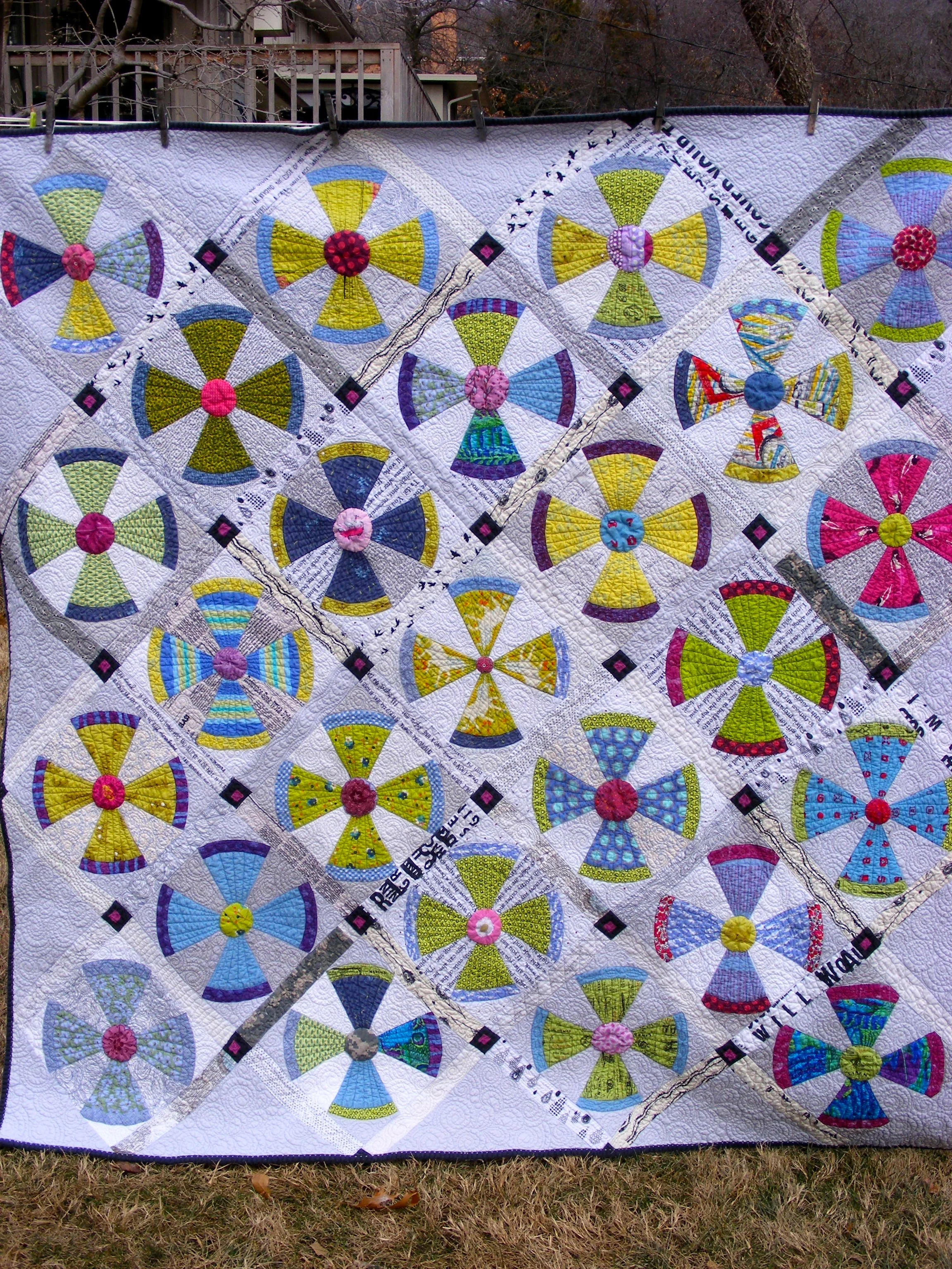 Colorful pattern quilt with circular and triangular designs hanging outdoors.