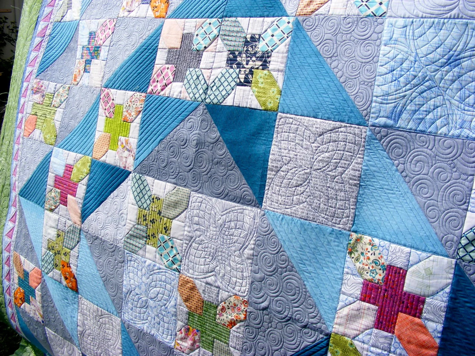 Colorful patchwork quilt with various geometric and floral patterns, dominated by blue tones and featuring intricate stitching.