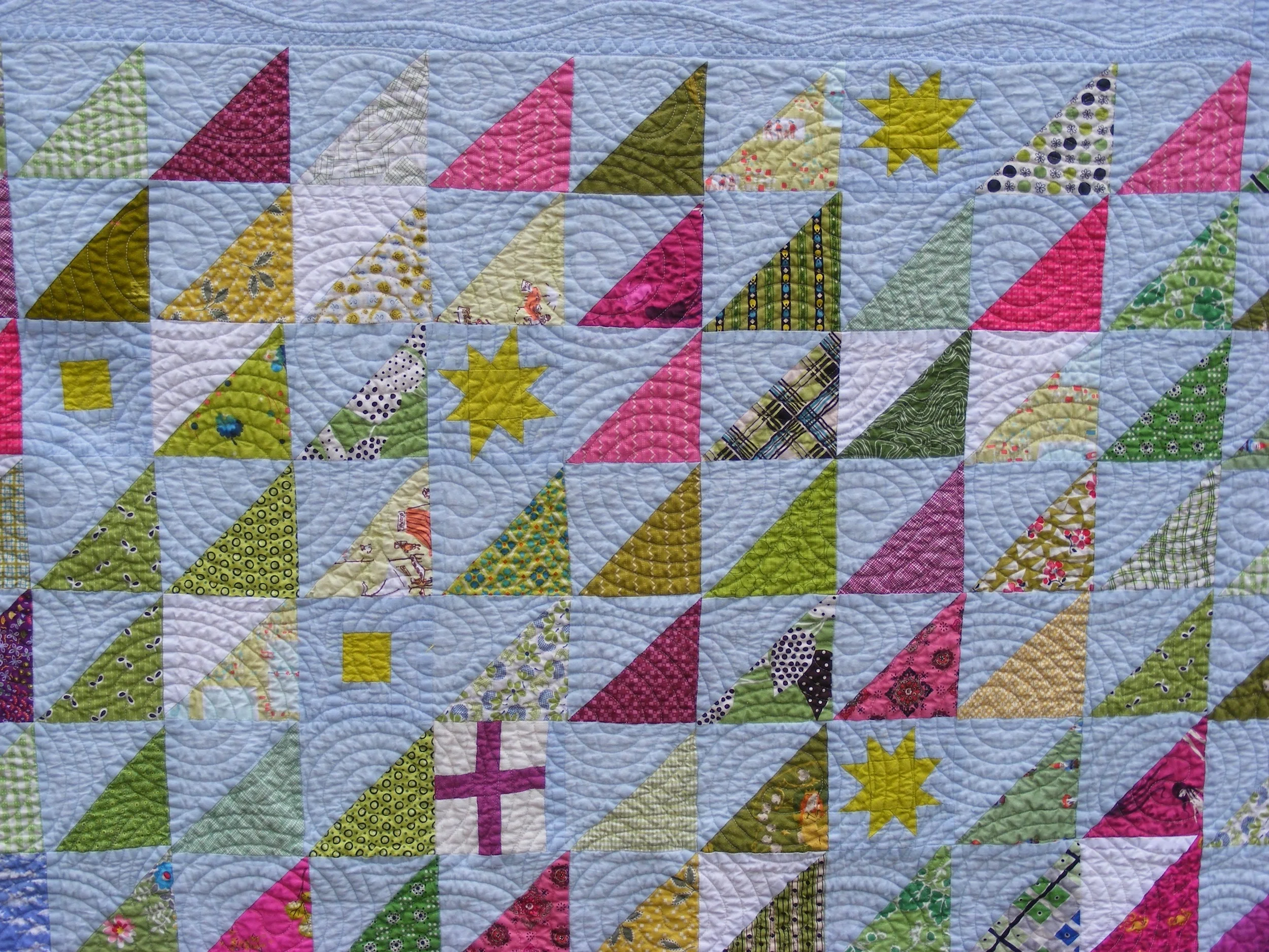 Colorful quilt with geometric patterns and patchwork triangles in various shades of pink, green, and yellow on a light background.