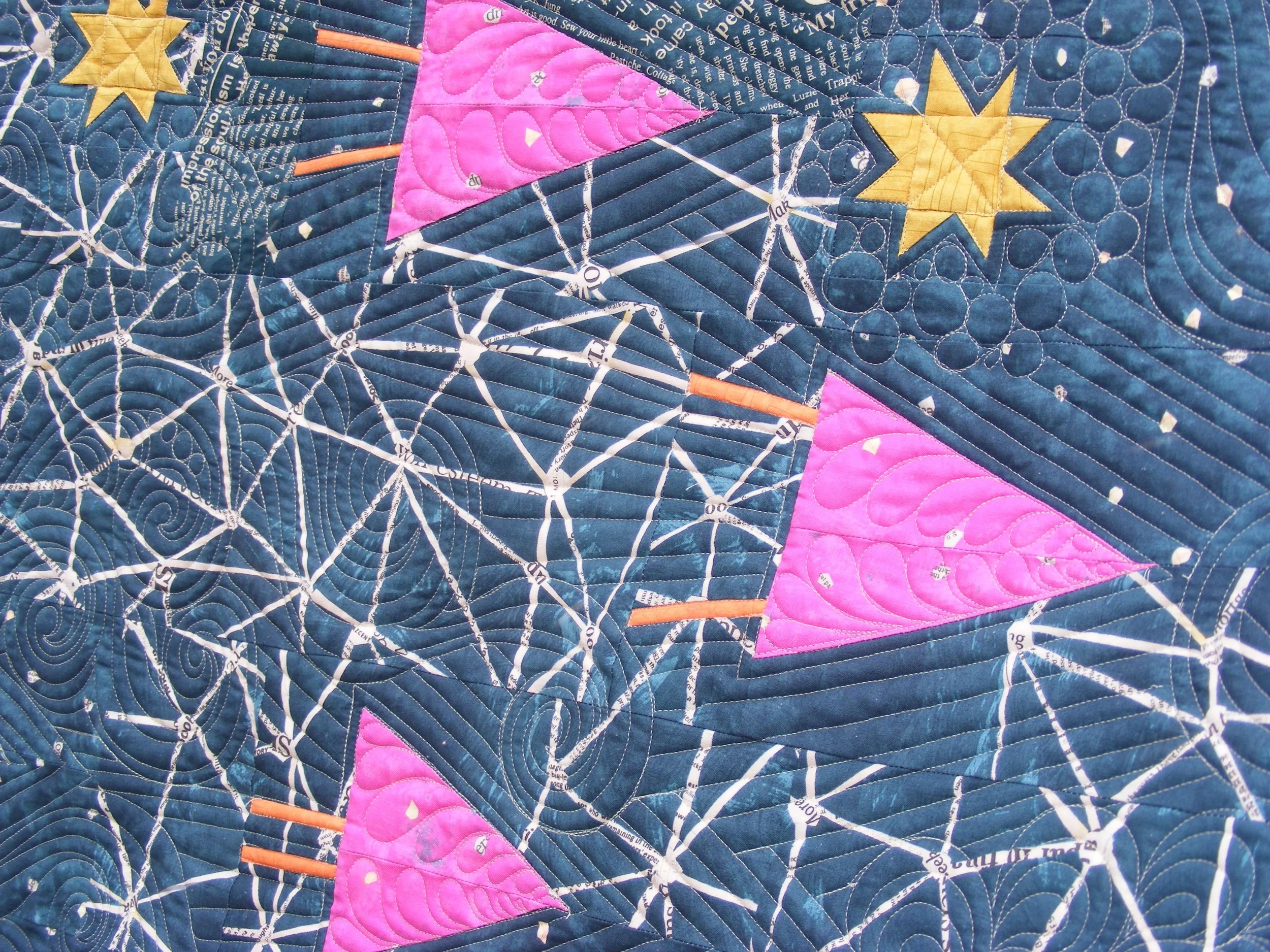 Colorful quilt featuring geometric patterns, including yellow stars, pink triangles, and white lines resembling constellations on a dark blue background.
