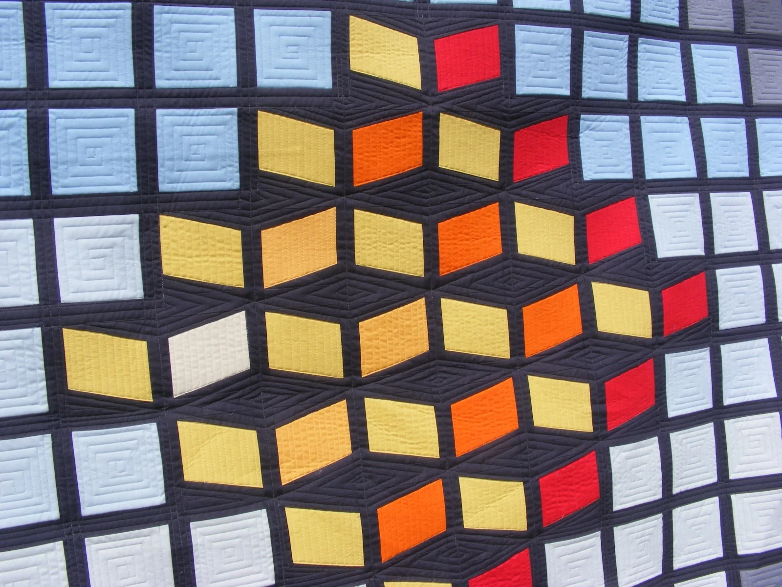 Colorful quilt pattern with geometric shapes and squares in blue, yellow, orange, and red.