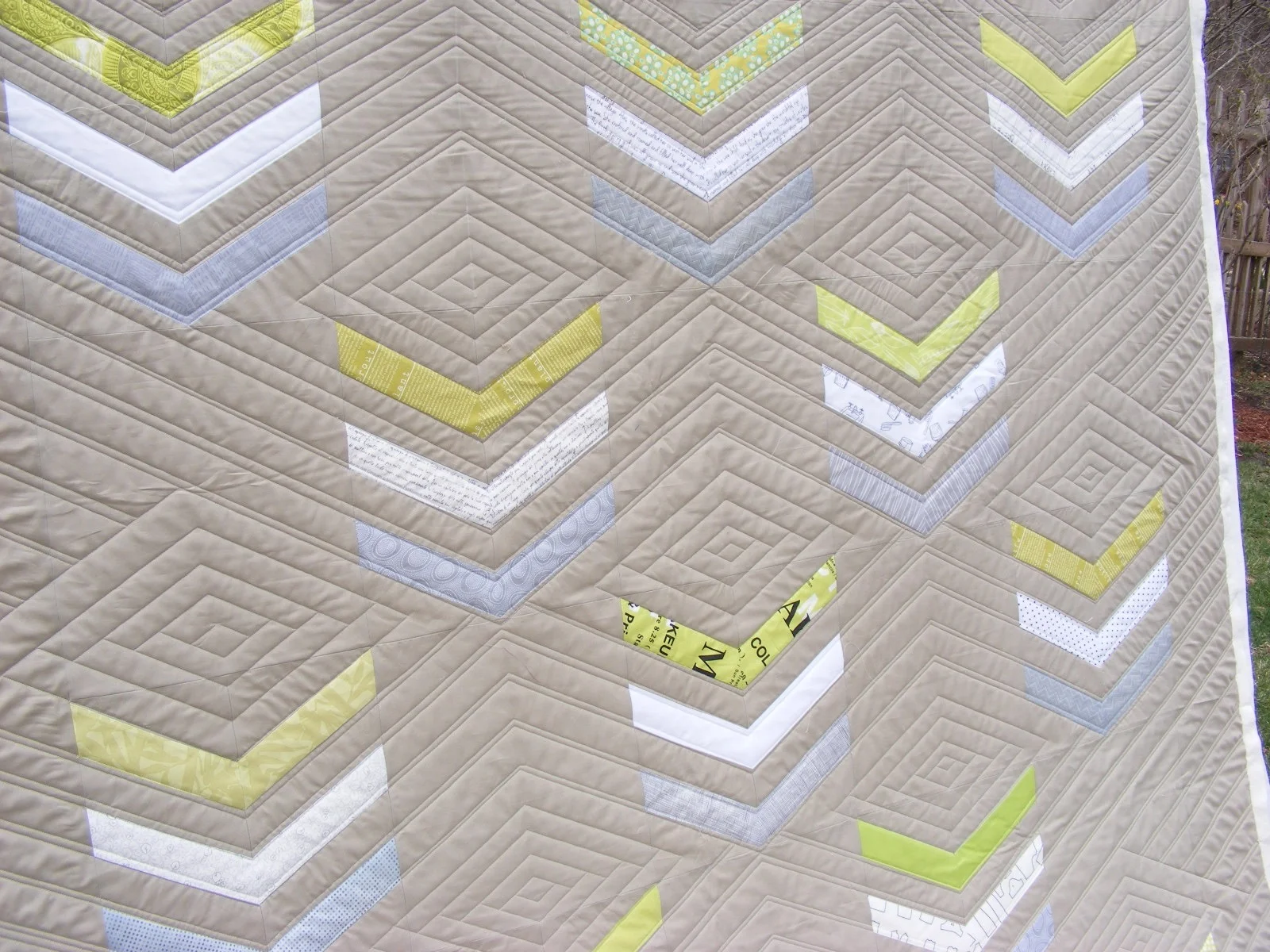 Quilt with geometric chevron patterns in shades of beige, gray, yellow, and white.
