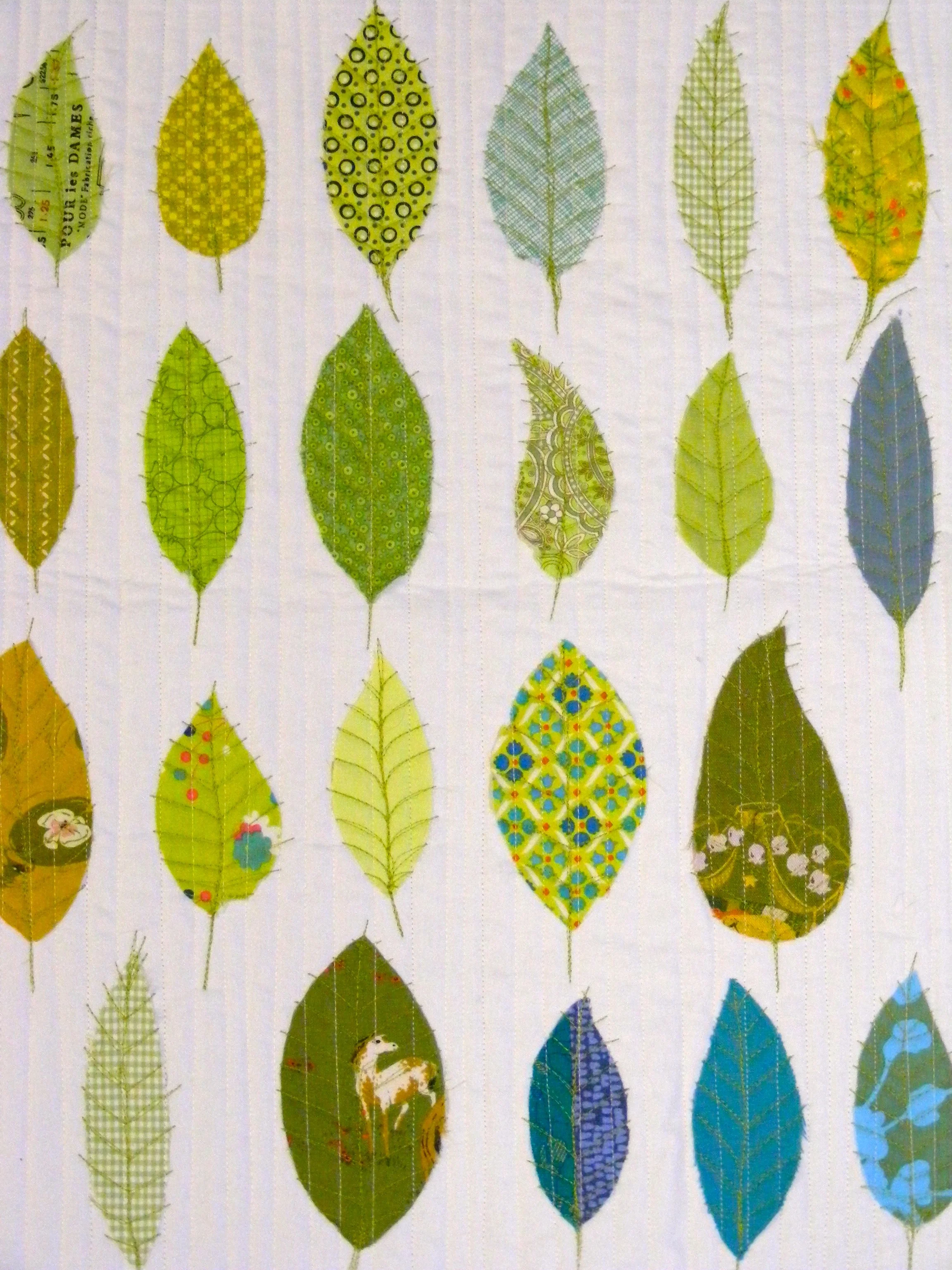 Quilt with patterned leaves on white background, featuring various green, yellow, and blue designs.