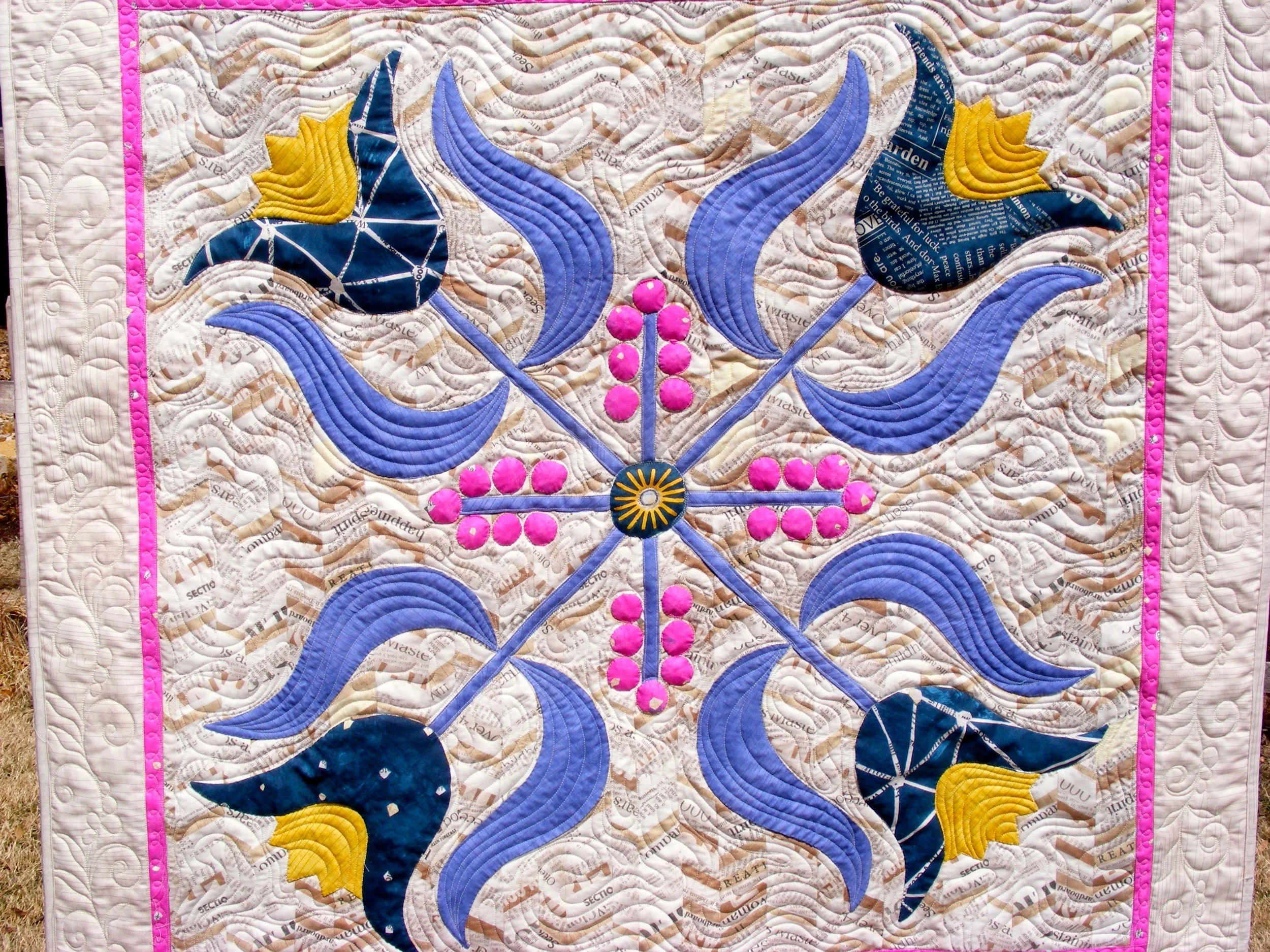 Colorful quilt with floral pattern, featuring blue and yellow flowers, pink accents, and decorative stitching.
