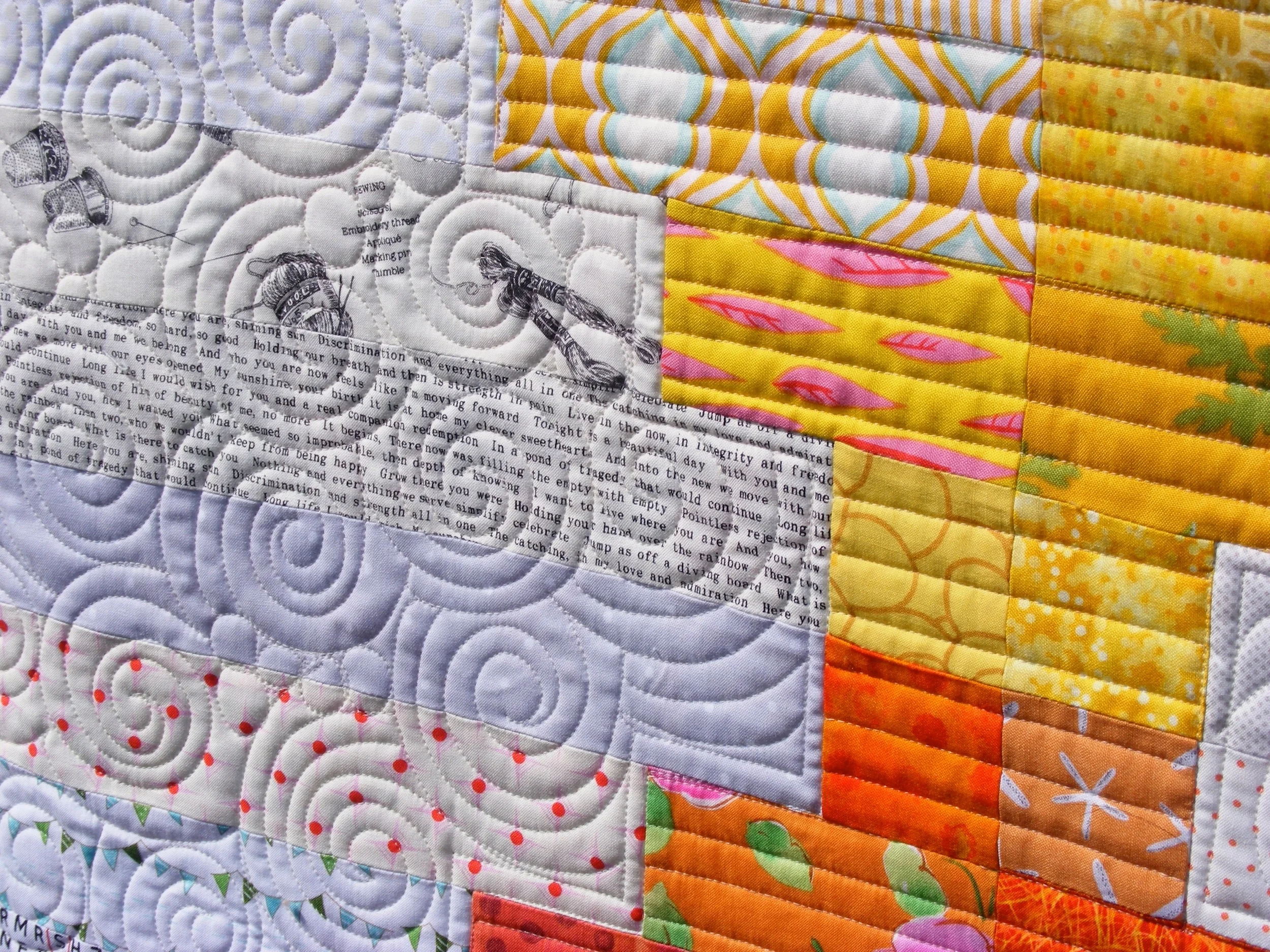 Colorful patchwork quilt with various geometric patterns, swirls, and text elements in shades of white, yellow, orange, and pink.