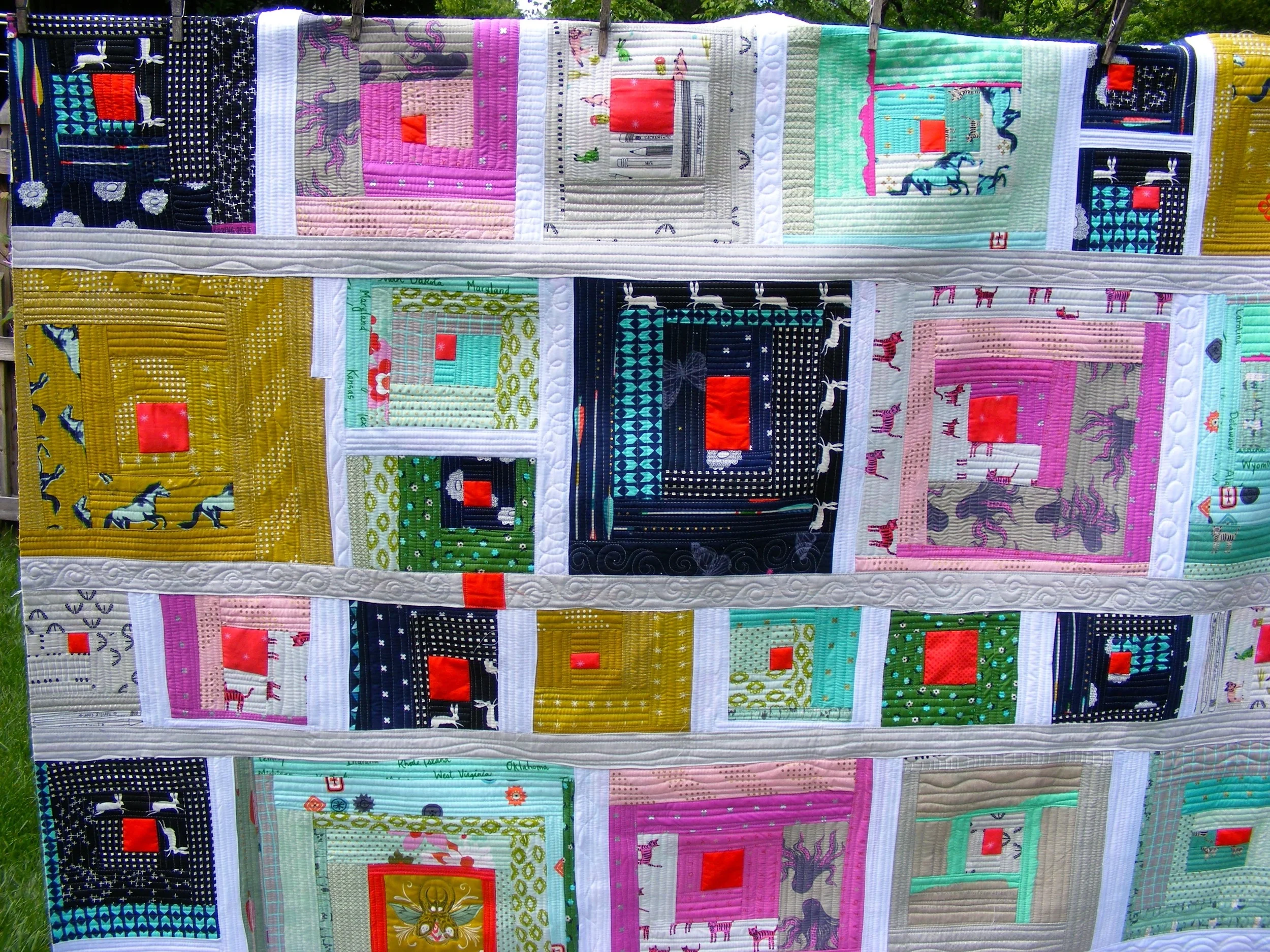 Colorful patchwork quilt with various patterned and solid fabric squares featuring red centers, displayed outdoors.