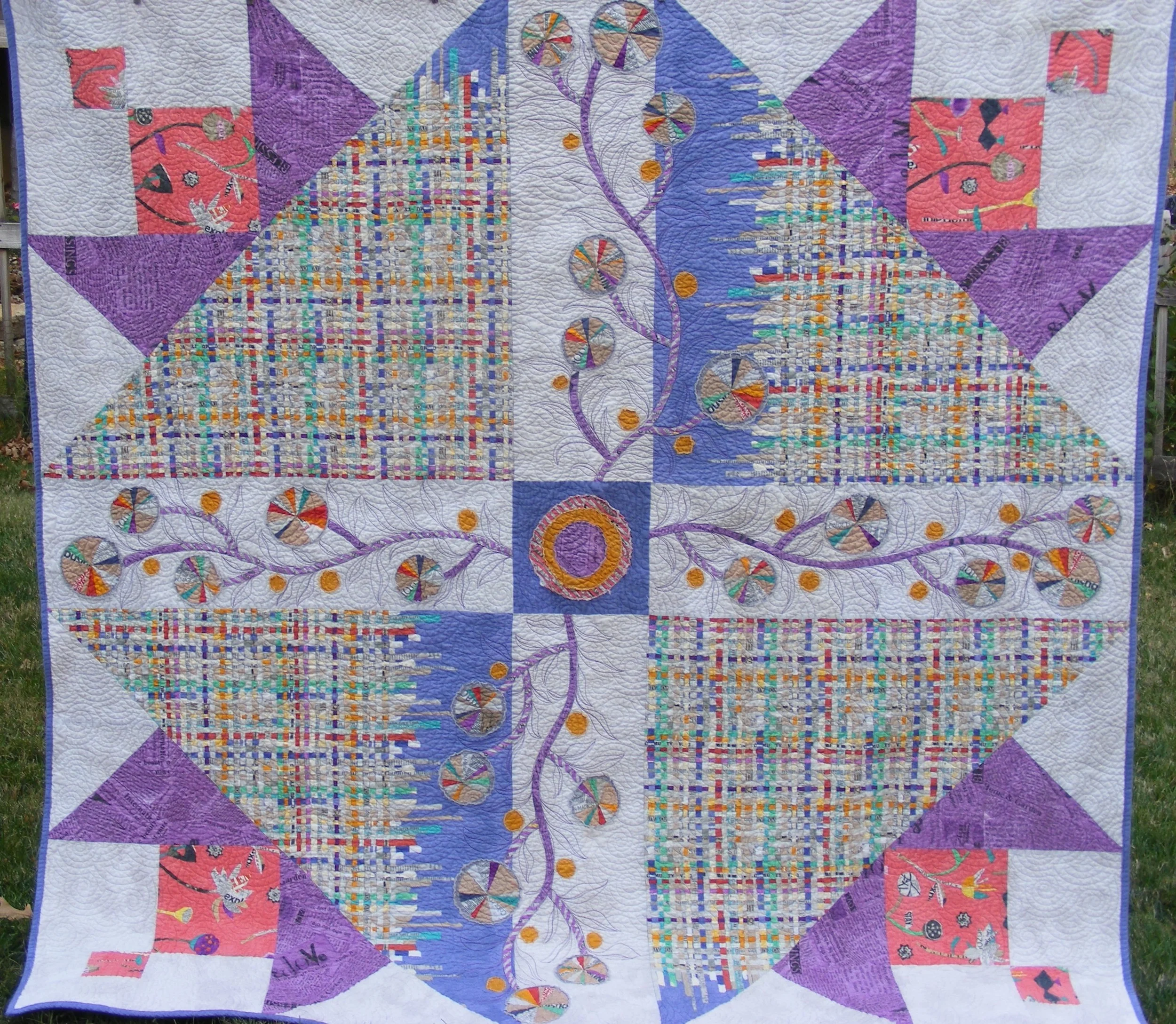 Patchwork quilt with colorful geometric and floral patterns, including purple triangles, multicolored woven-like designs, and circular floral motifs on a white background.