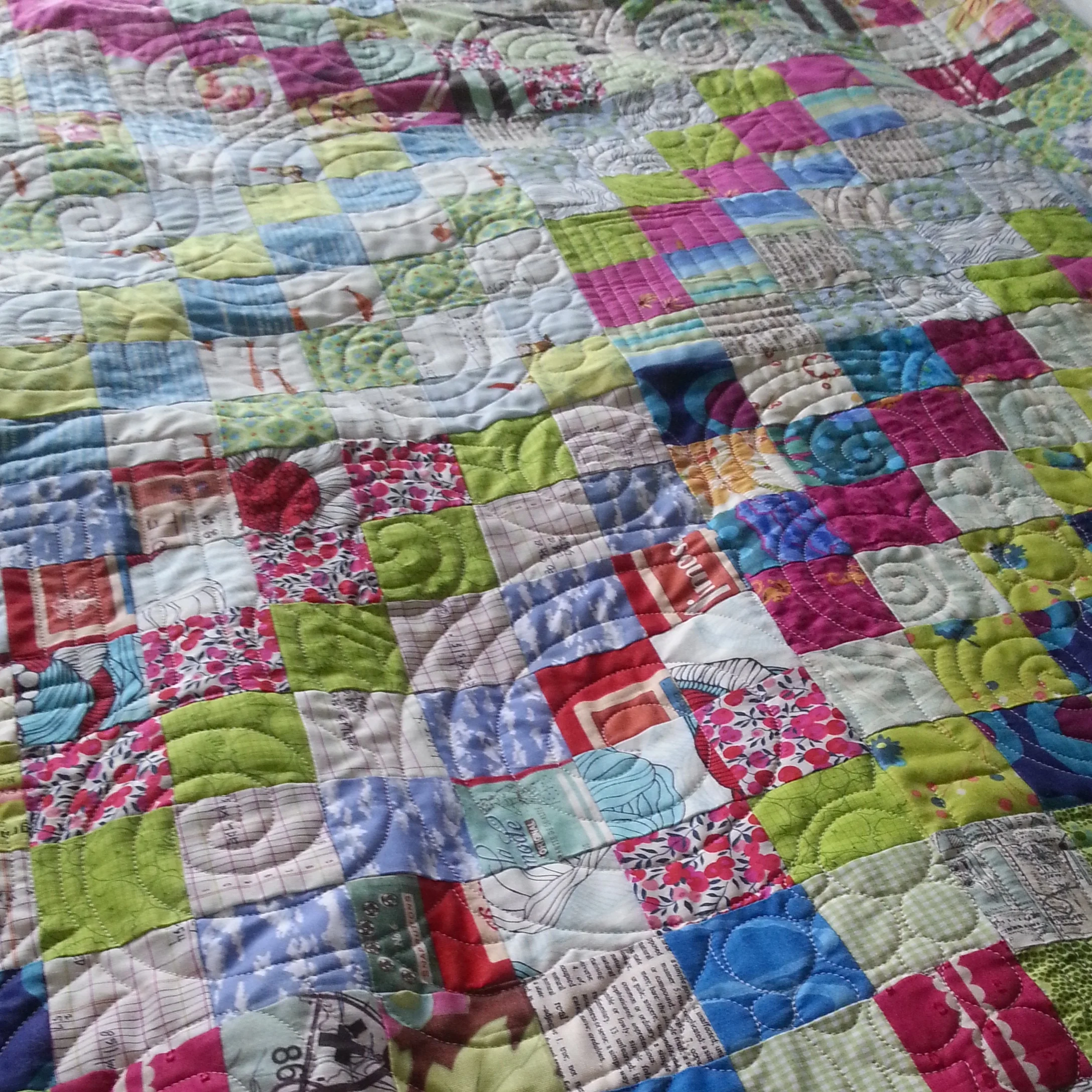 Colorful patchwork quilt with various fabric patterns and quilted swirls.