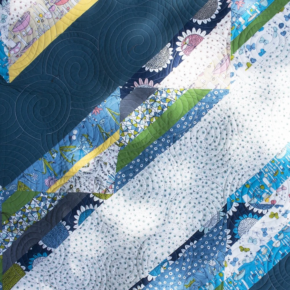 Patchwork quilt with colorful fabric strips in diagonal patterns, featuring floral and geometric designs.