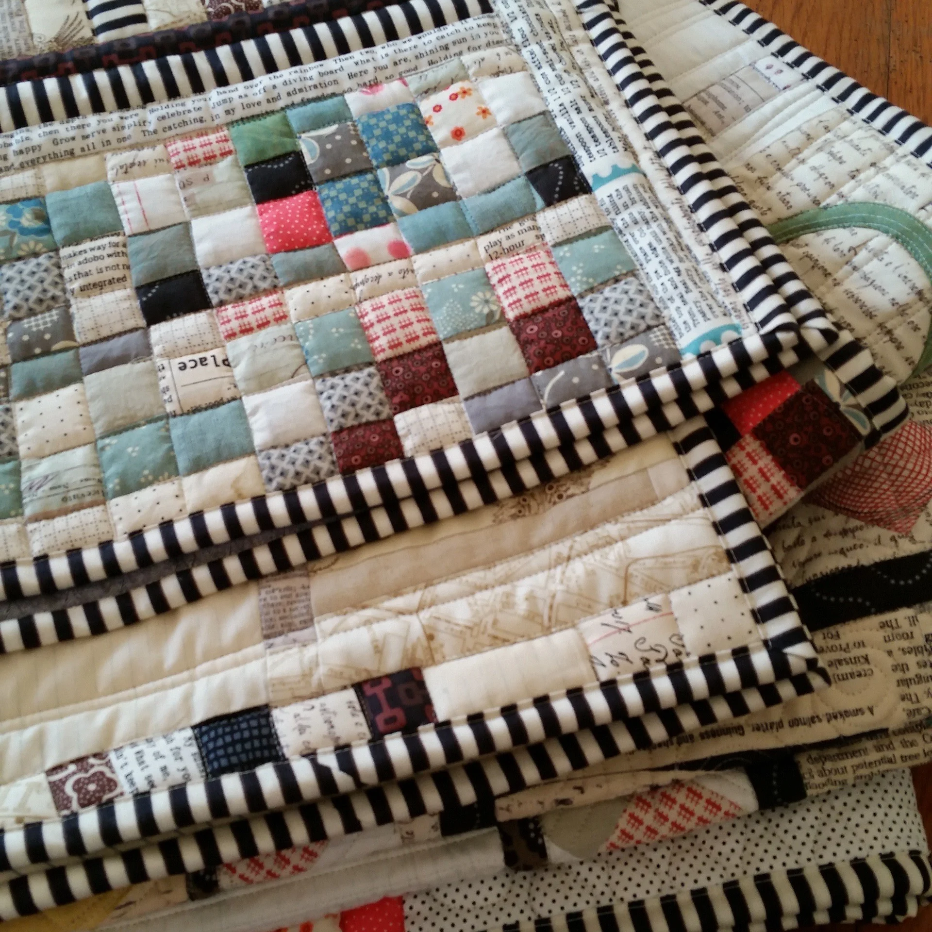Stack of patchwork quilts with striped edging on a wooden surface