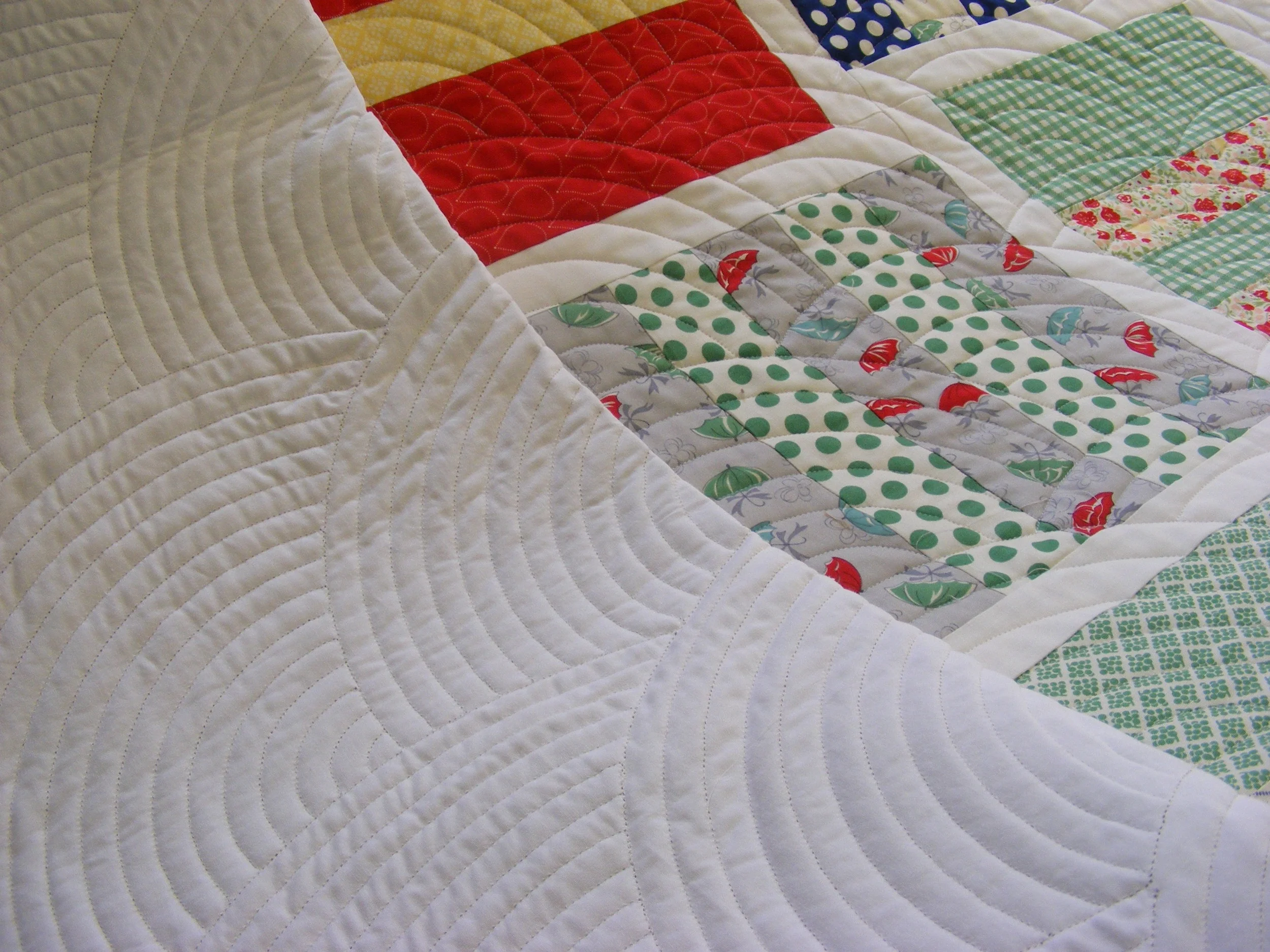 Patchwork quilt with various colored fabrics, including red, green polka dots, and geometric patterns, featuring wavy quilting stitches.