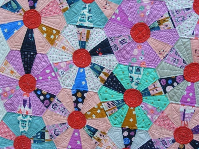 Colorful quilt pattern featuring hexagonal shapes in various pastel colors and designs, each with a circular red center.