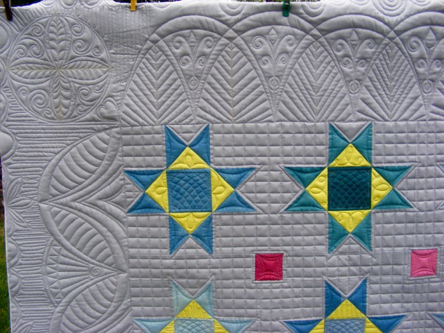 A detailed patchwork quilt featuring star patterns in blue and yellow, with intricate quilted designs and geometric shapes.