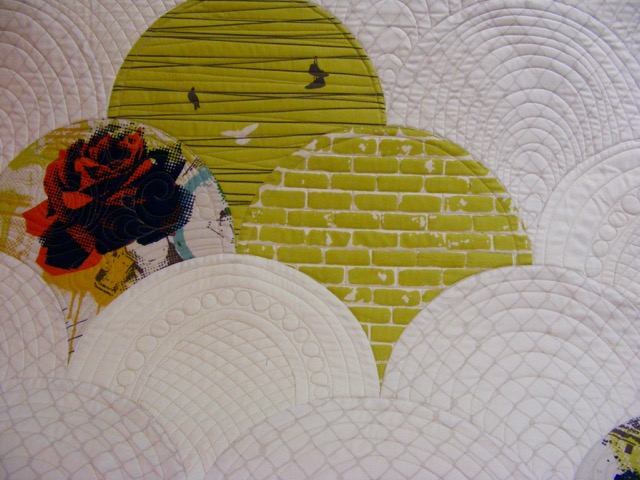 Quilt with colorful circular patterns, including a brick wall design, a red rose, and concentric arc stitching.