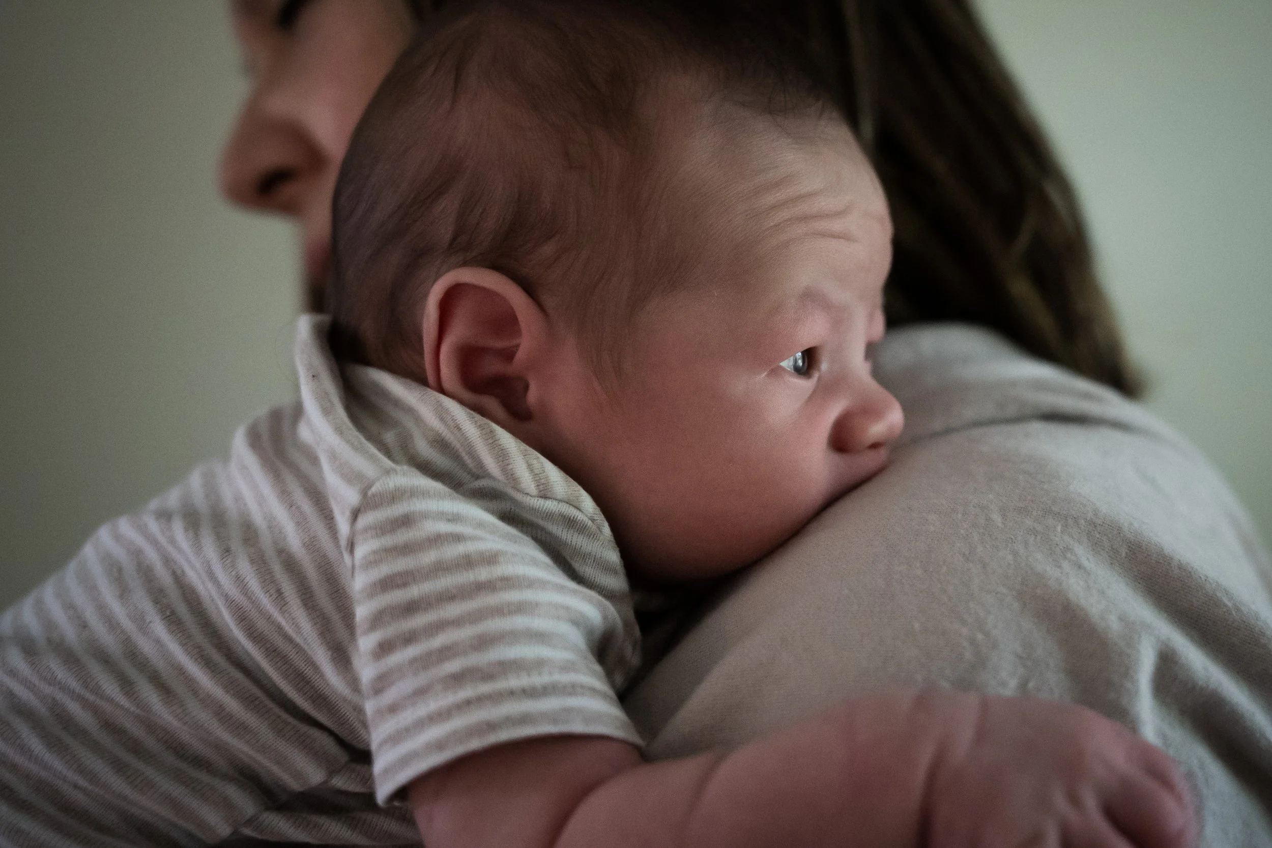 Close-up of a baby being held by an adult, focusing on the baby's head and profile as the baby rests on the adult's shoulder.