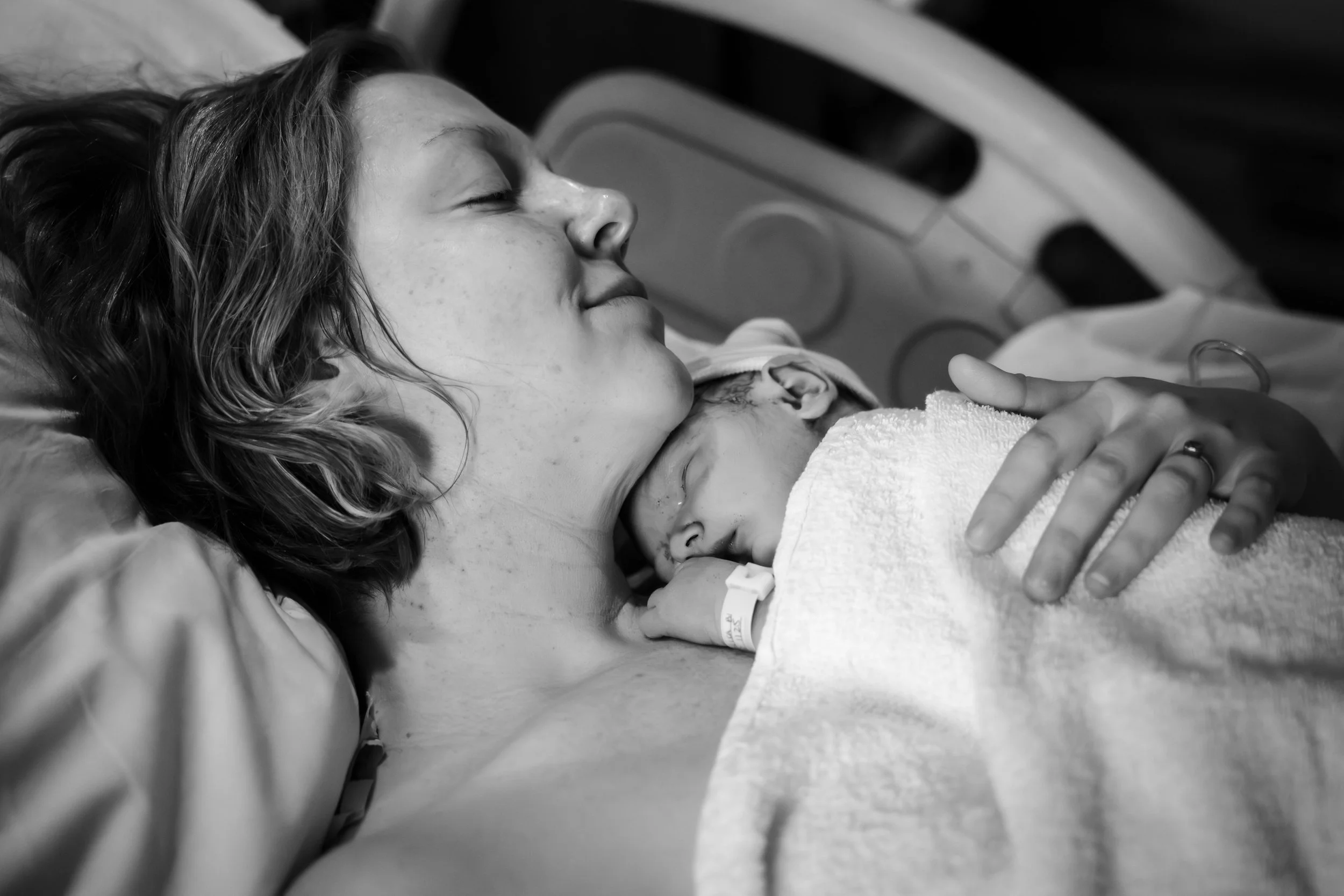 A new mother lying in a hospital bed, holding the hand of her newborn baby after birth. She is relieved and exhausted from giving birth.