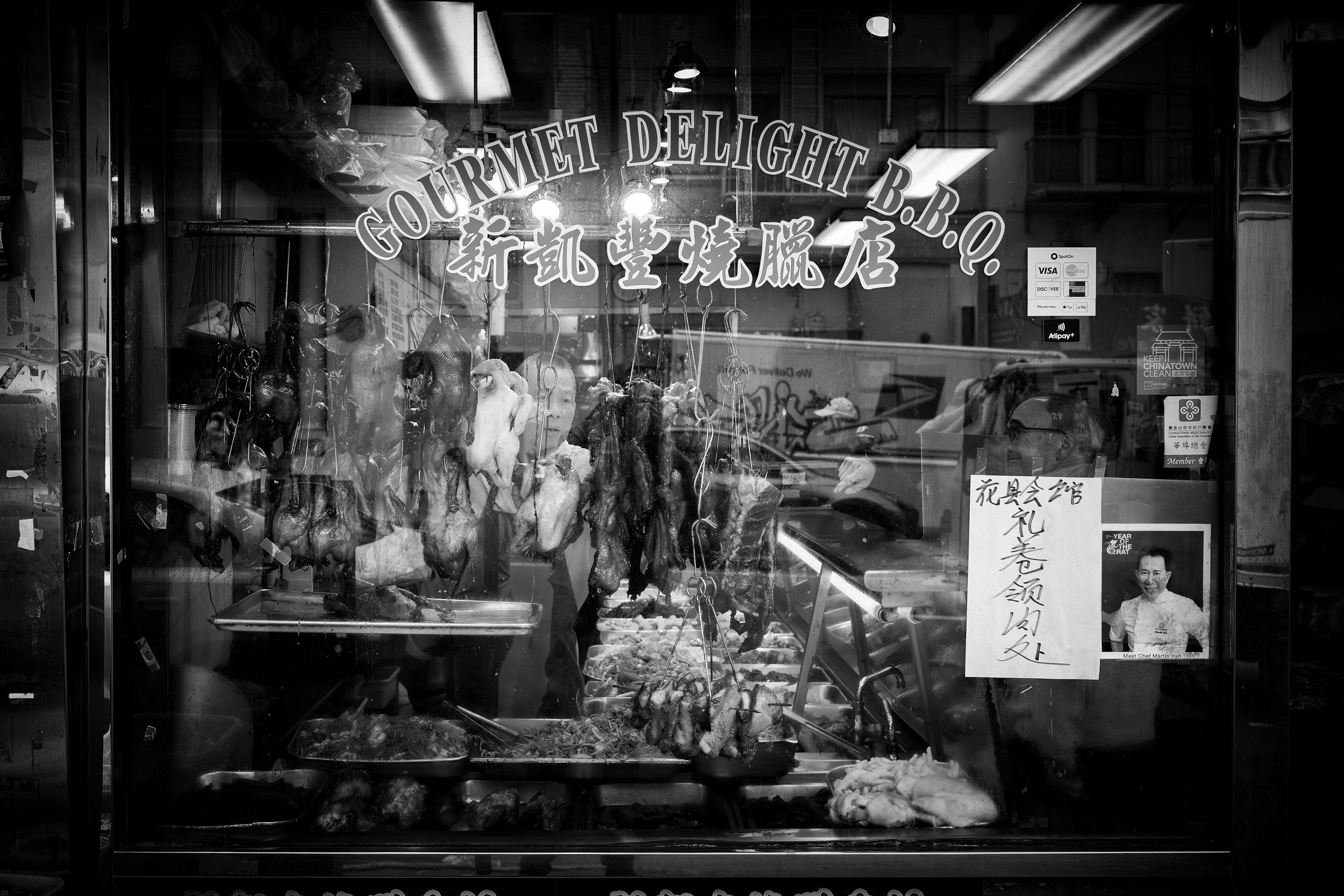 Gourmet Delight B.B.Q.

 

  The window of Gourmet Delight B.B.Q. in San Francisco's Chinatown is filled with hanging meats, signs, reflections, and activity from the street. The storefront is part of the neighborhood's dense restaurant and market la