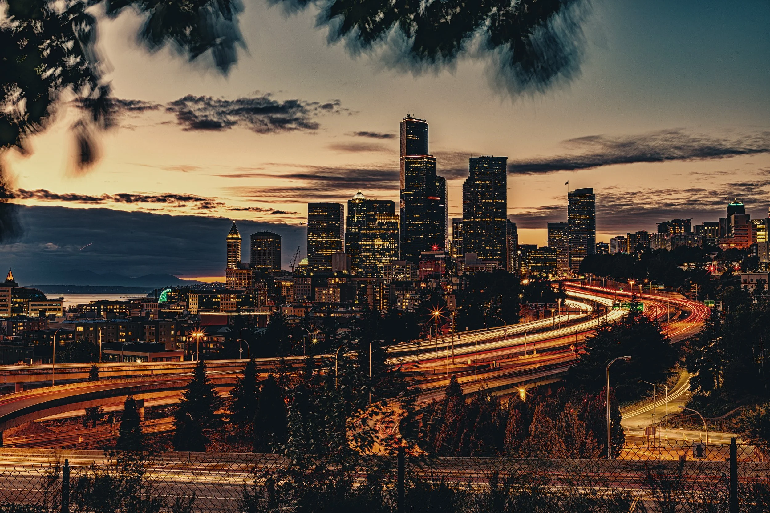 Seattle Skyline After Sunset

 

 Seattle's downtown skyline is shown after sunset with illuminated towers and freeway corridors below. The image includes the city's dense central skyline and transportation network. 