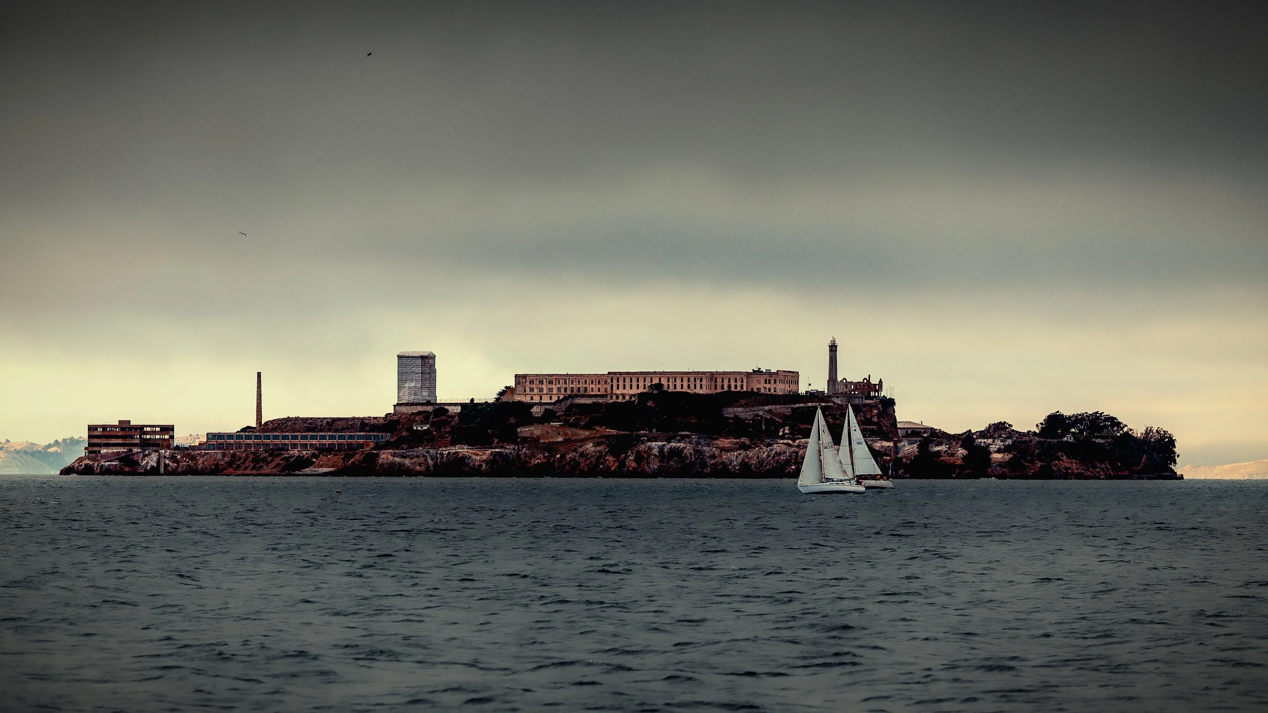 Alcatraz Island in San Francisco Bay beneath dark storm clouds.

 

 Alcatraz Island sits in San Francisco Bay between San Francisco and the Marin Headlands. The island is known for its former federal penitentiary, military history, and current role 