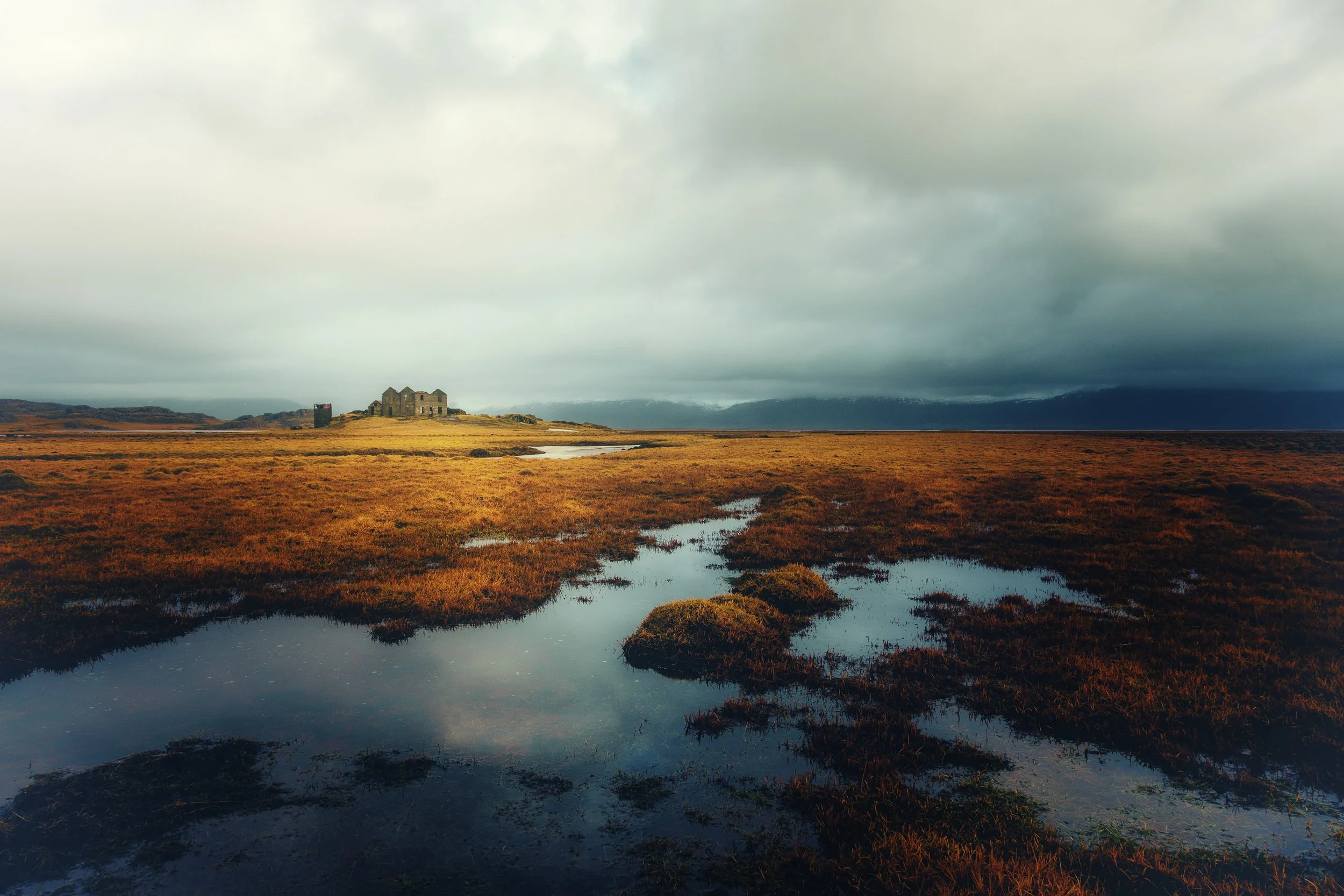 Abandoned structure on an open Icelandic plain with reflective water, distant mountains, and dramatic clouds