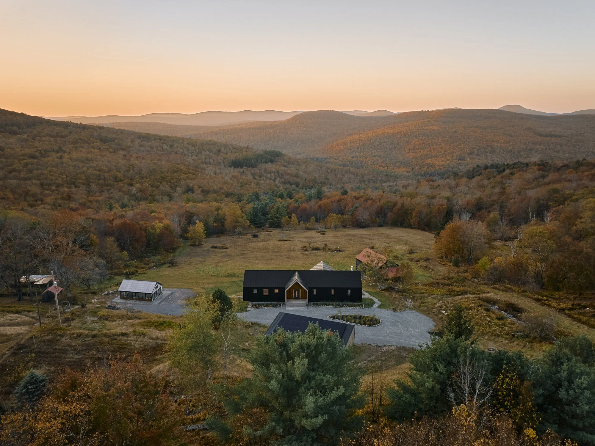 Aerial view of a mountain landscape during sunset with a modern black house and surrounding trees in autumn colors.