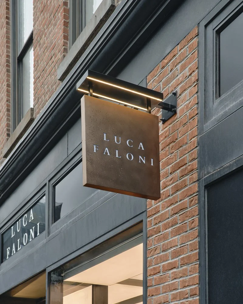 Storefront with a hanging sign that reads 'Luca Faloni' against a brick exterior wall.