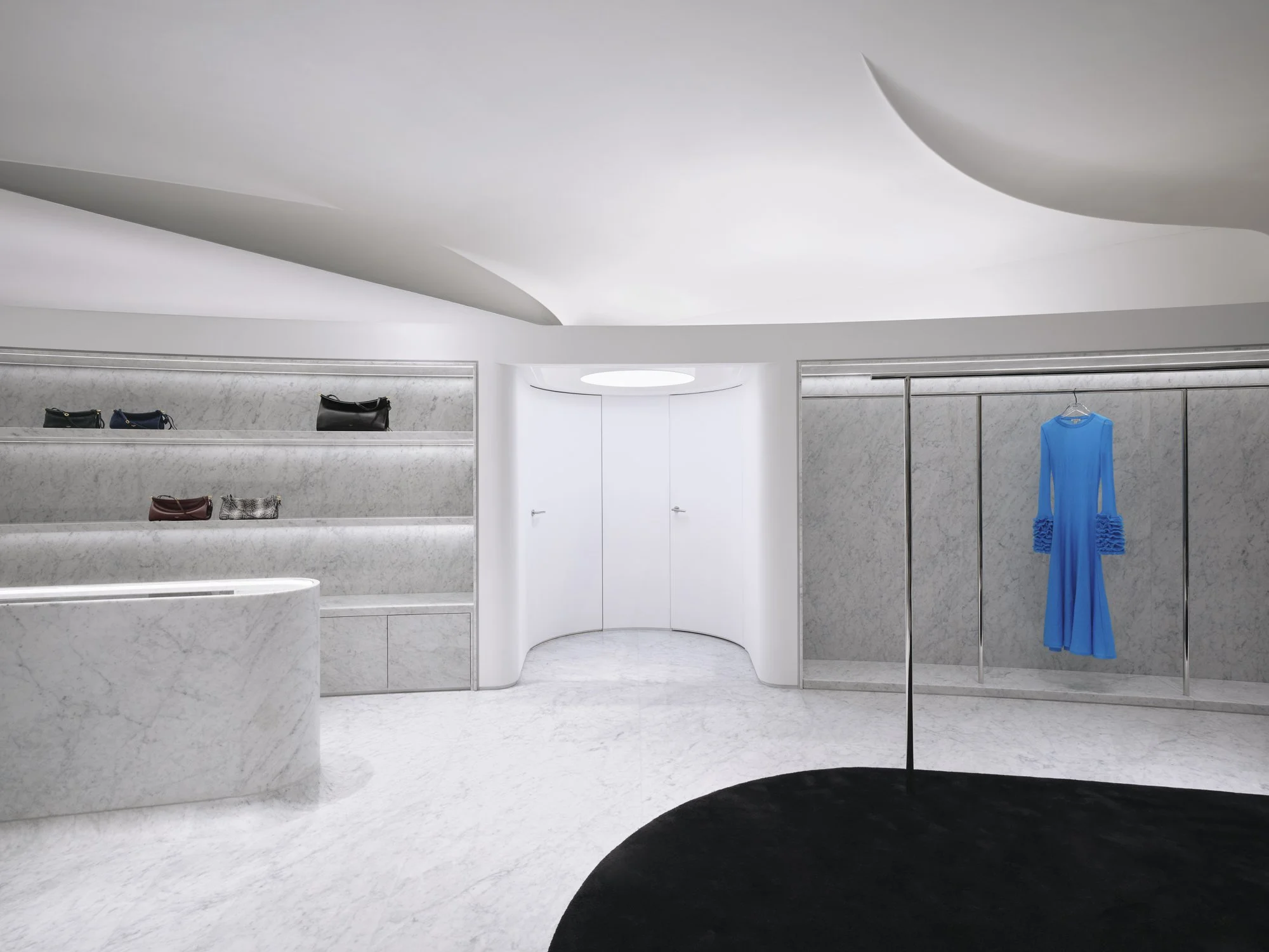 A minimalist boutique interior with marble display shelves holding handbags and a clothing rack with a bright blue dress.