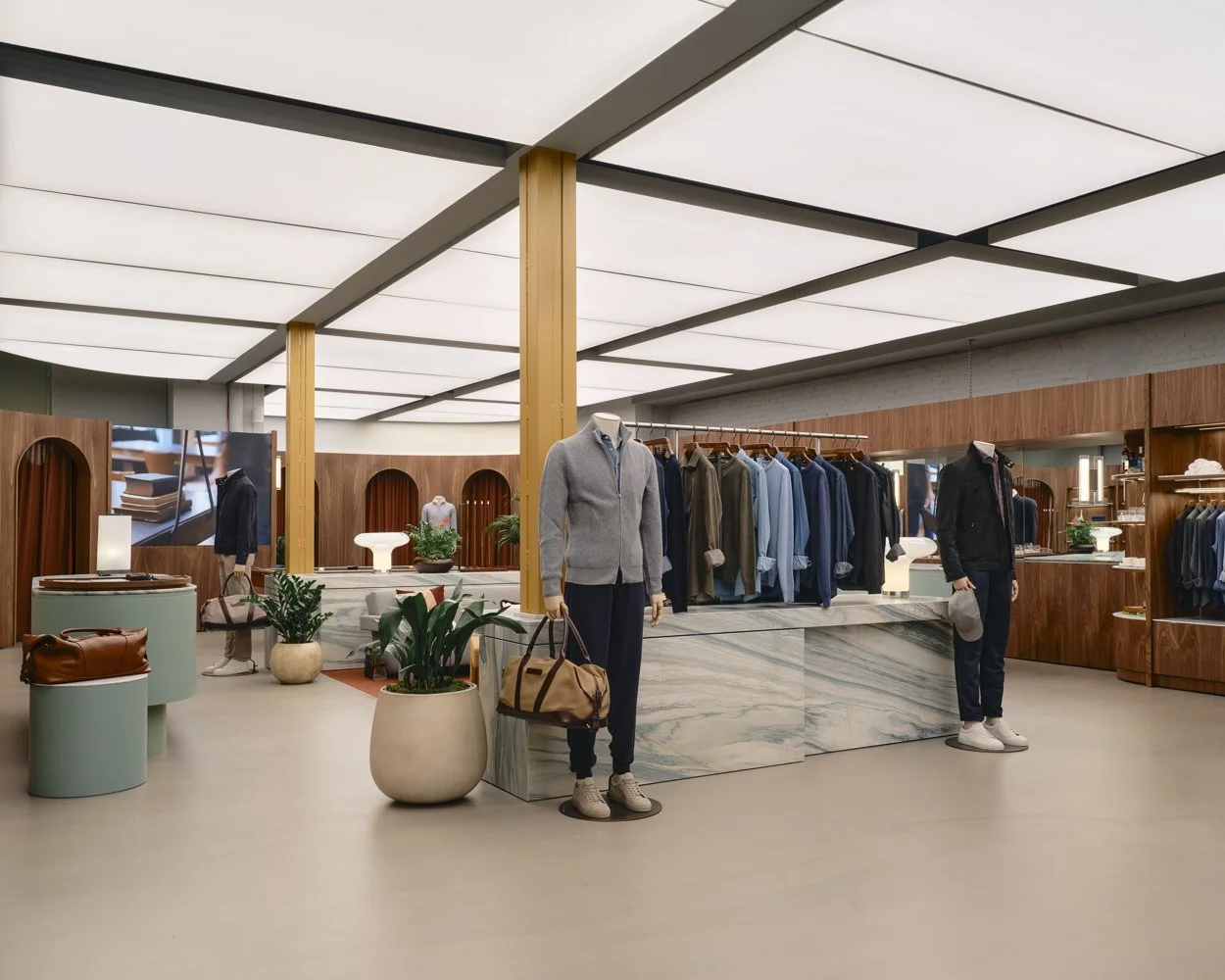 Inside a clothing store with mannequins dressed in casual outfits, a display of folded clothes, and wooden shelving. The store has a modern design with a high ceiling, potted plants, and warm lighting.
