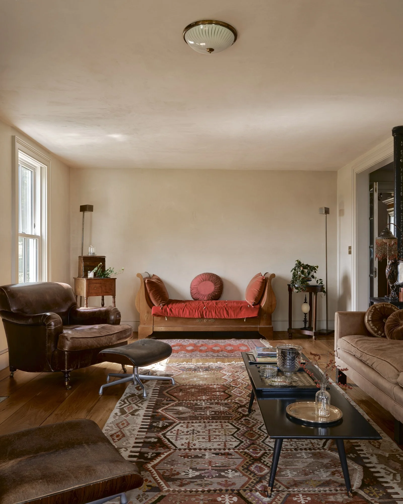 Living room with vintage furniture, wooden floor, area rug, window, and decorative plants.