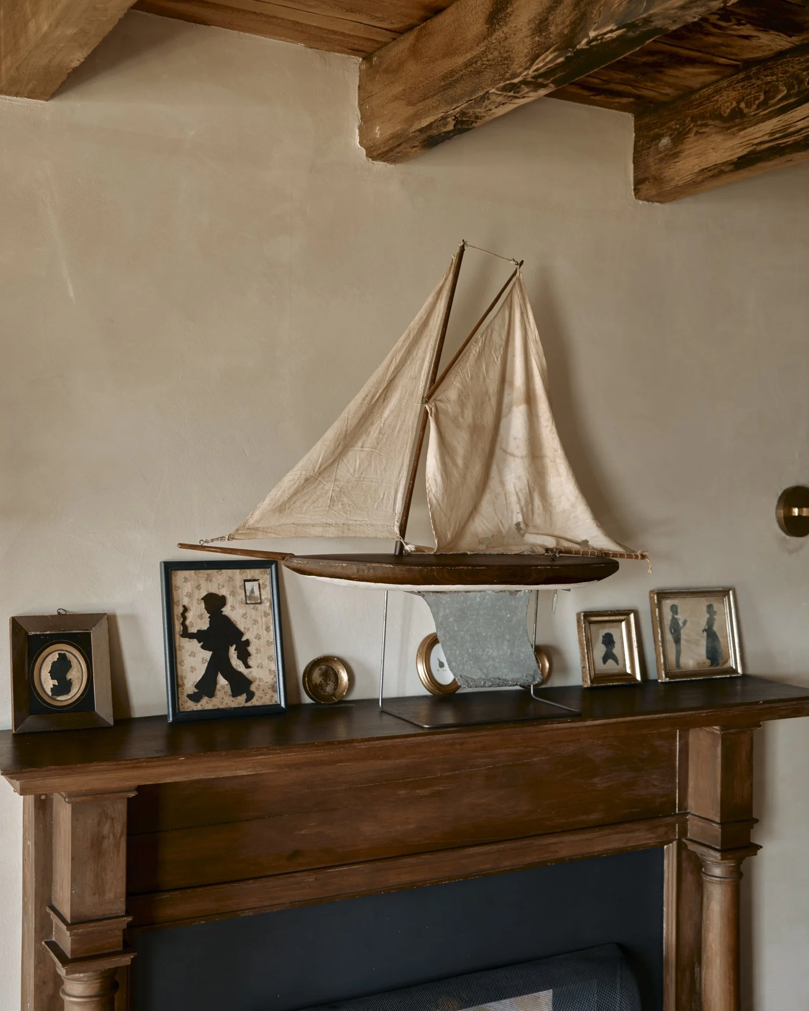 A wooden sailboat model on a fireplace mantel, surrounded by framed silhouettes of children and decorative items.