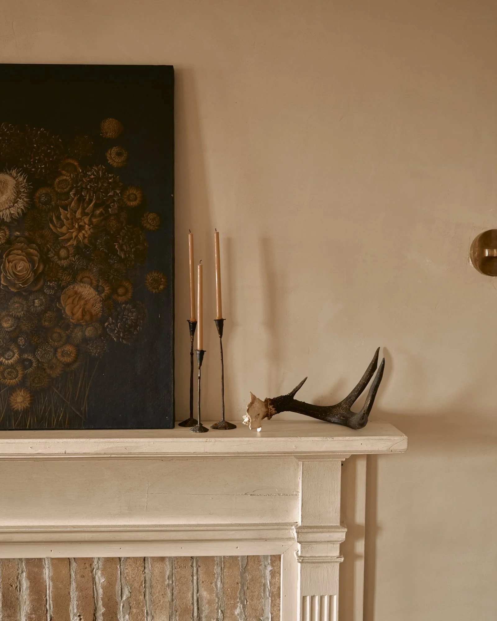 Decorative fireplace mantel with candles, antler, and framed artwork.