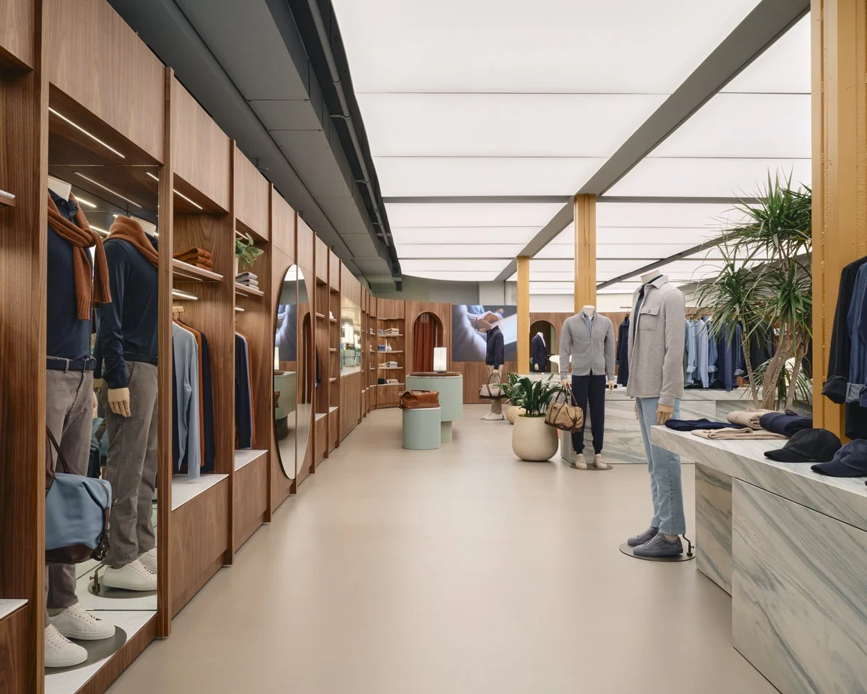Inside a clothing store with mannequins dressed in casual attire, wooden shelving units, potted plants, and a modern, minimalist design.