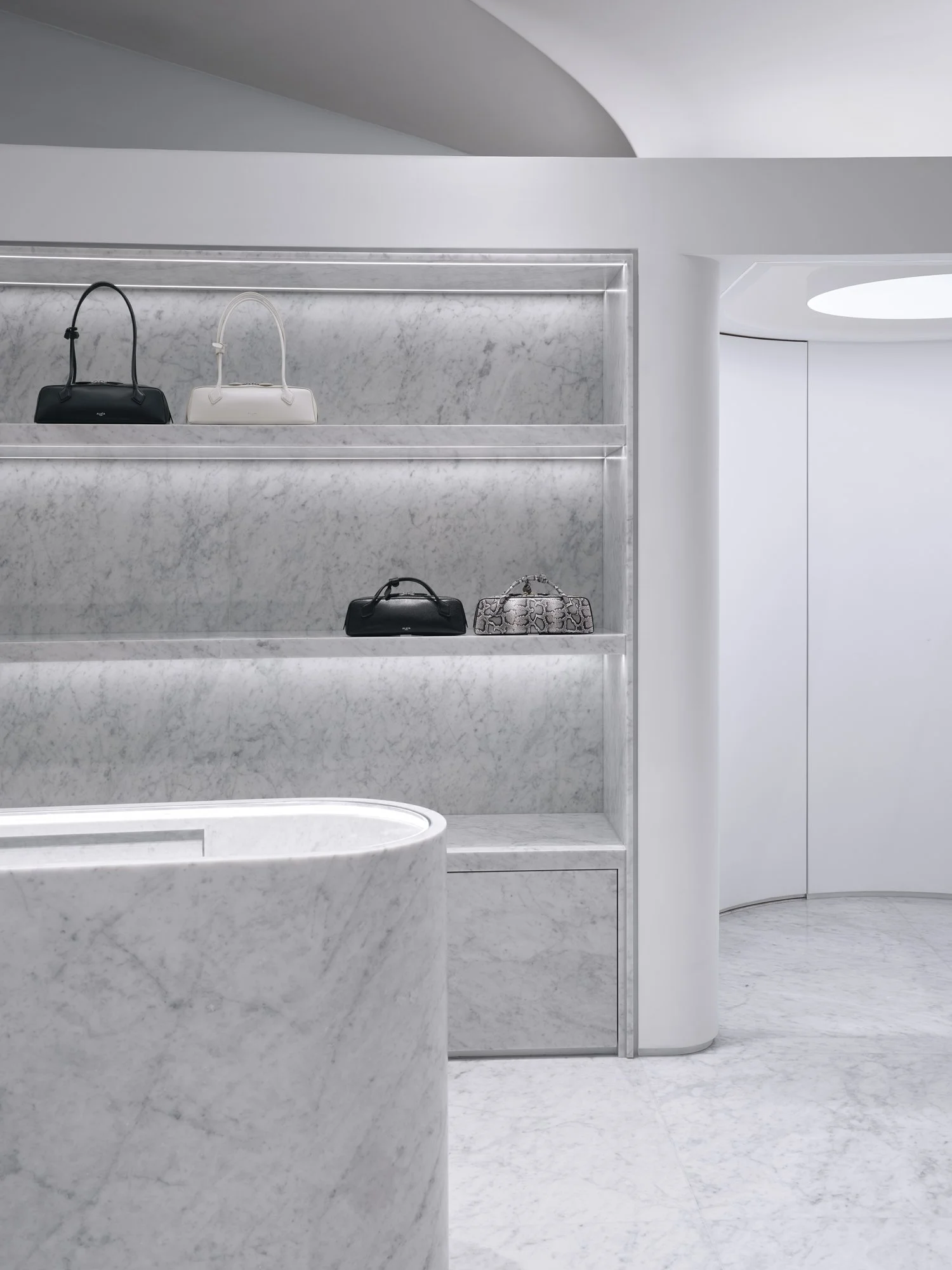 Display of handbags on marble shelves in a minimalistic, modern retail store with white curved walls and soft lighting.