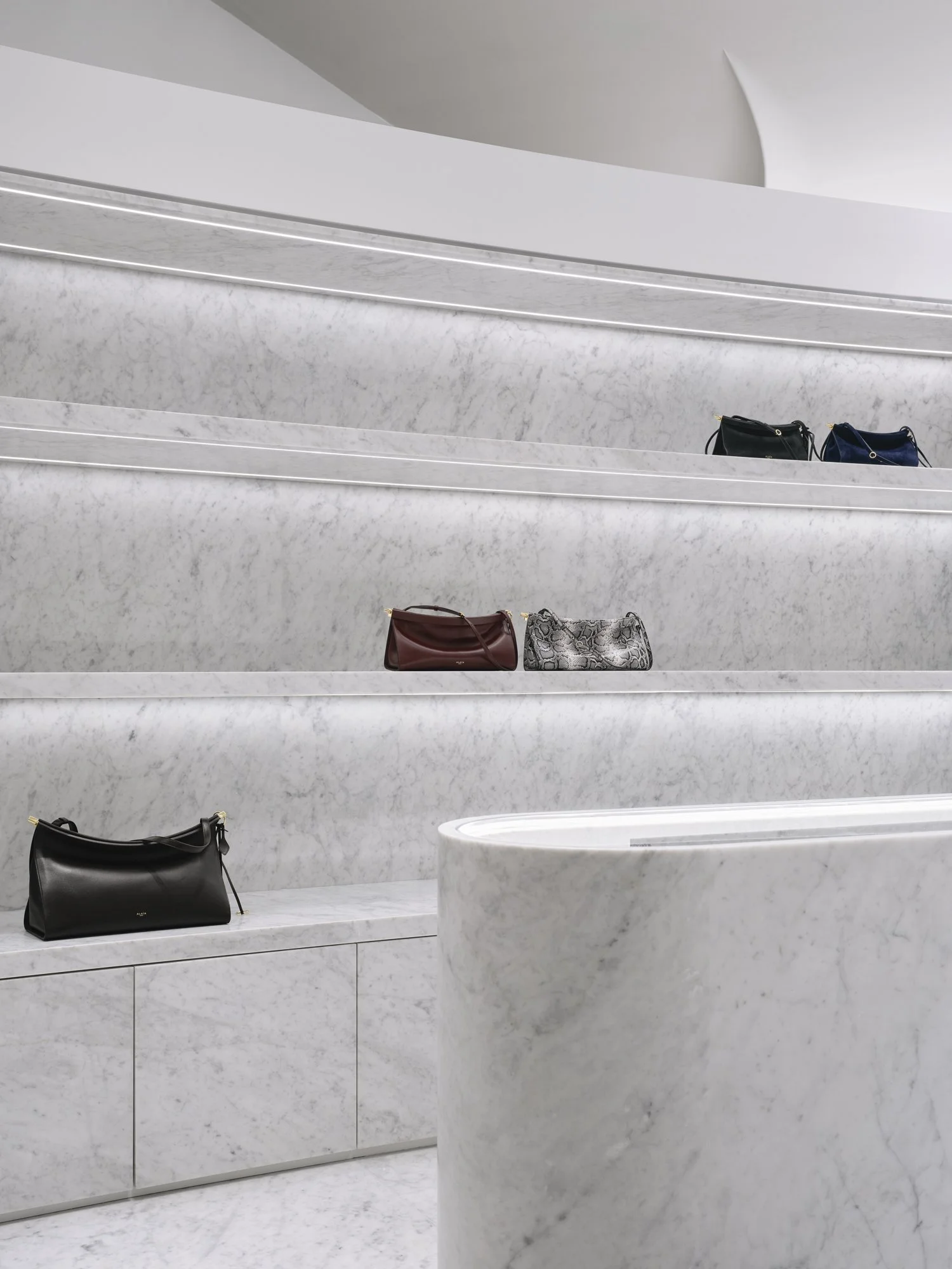 Display of handbags on marble shelves in a modern, minimalist store.