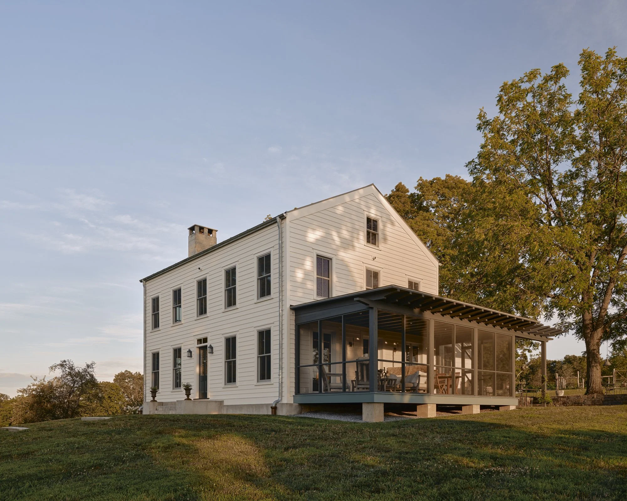 White two-story house with large screened porch, set on green lawn with trees, during sunset.