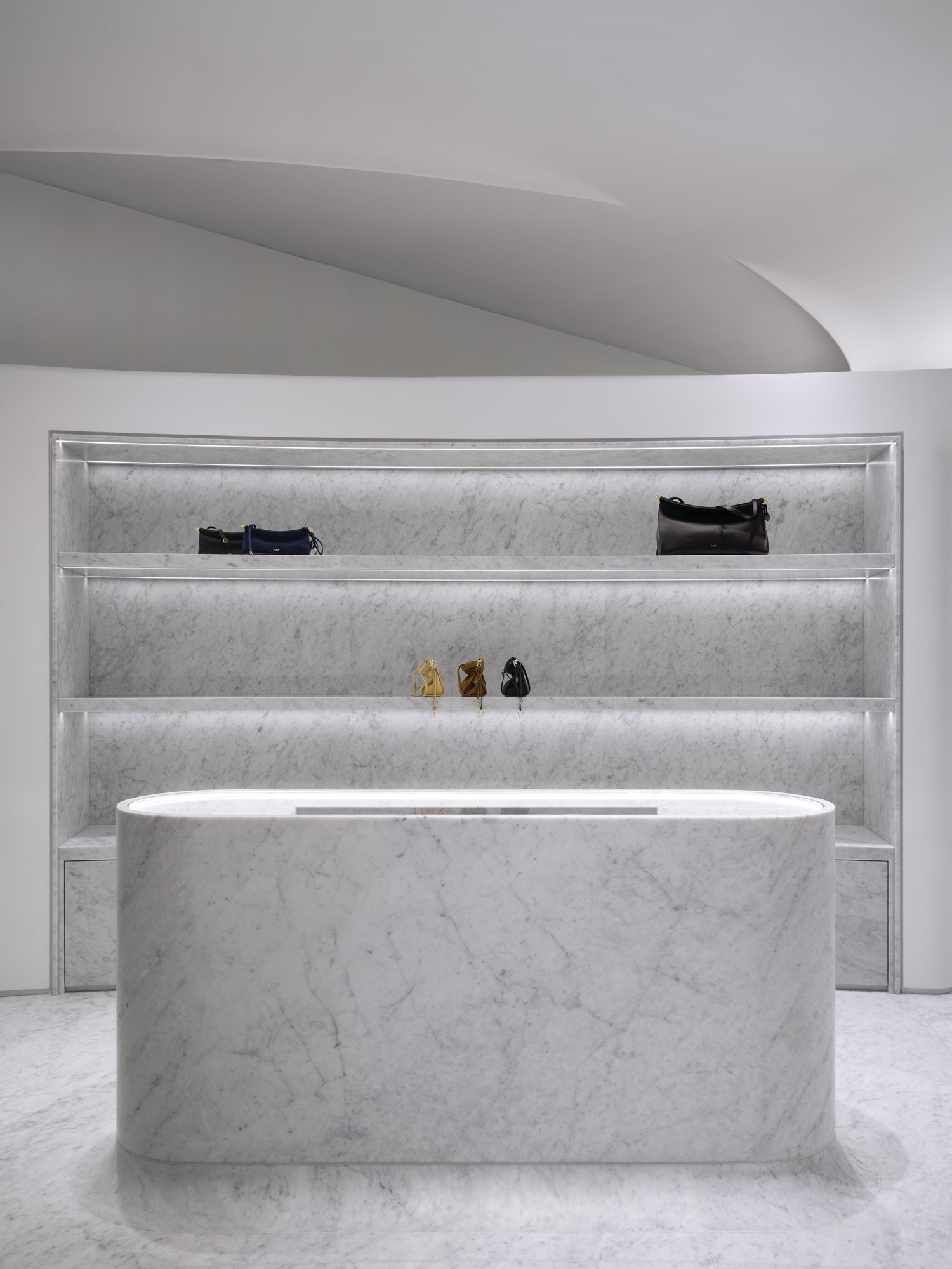Minimalist display with marble shelves and a marble counter, showcasing handbags in a retail store.